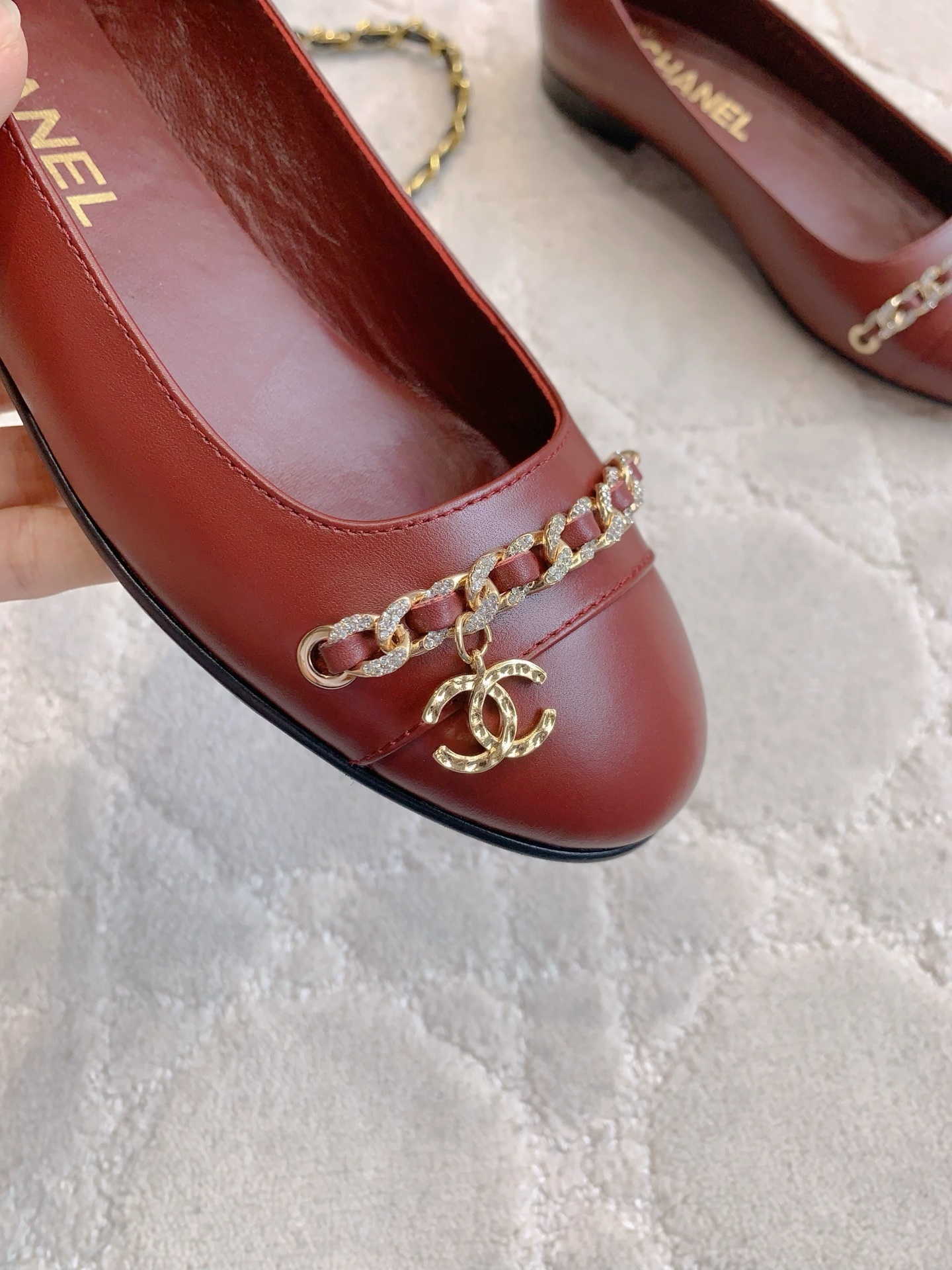 Luxury burgundy red Chanel leather ballet flats with gold chain and CC logo detail on a marble table. - Hình 7