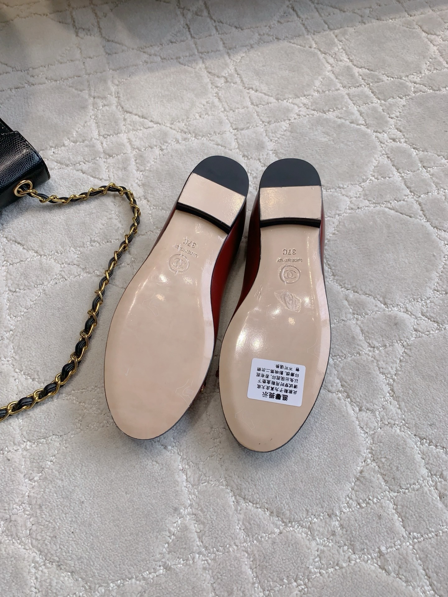 Luxury burgundy red Chanel leather ballet flats with gold chain and CC logo detail on a marble table. - Hình 6