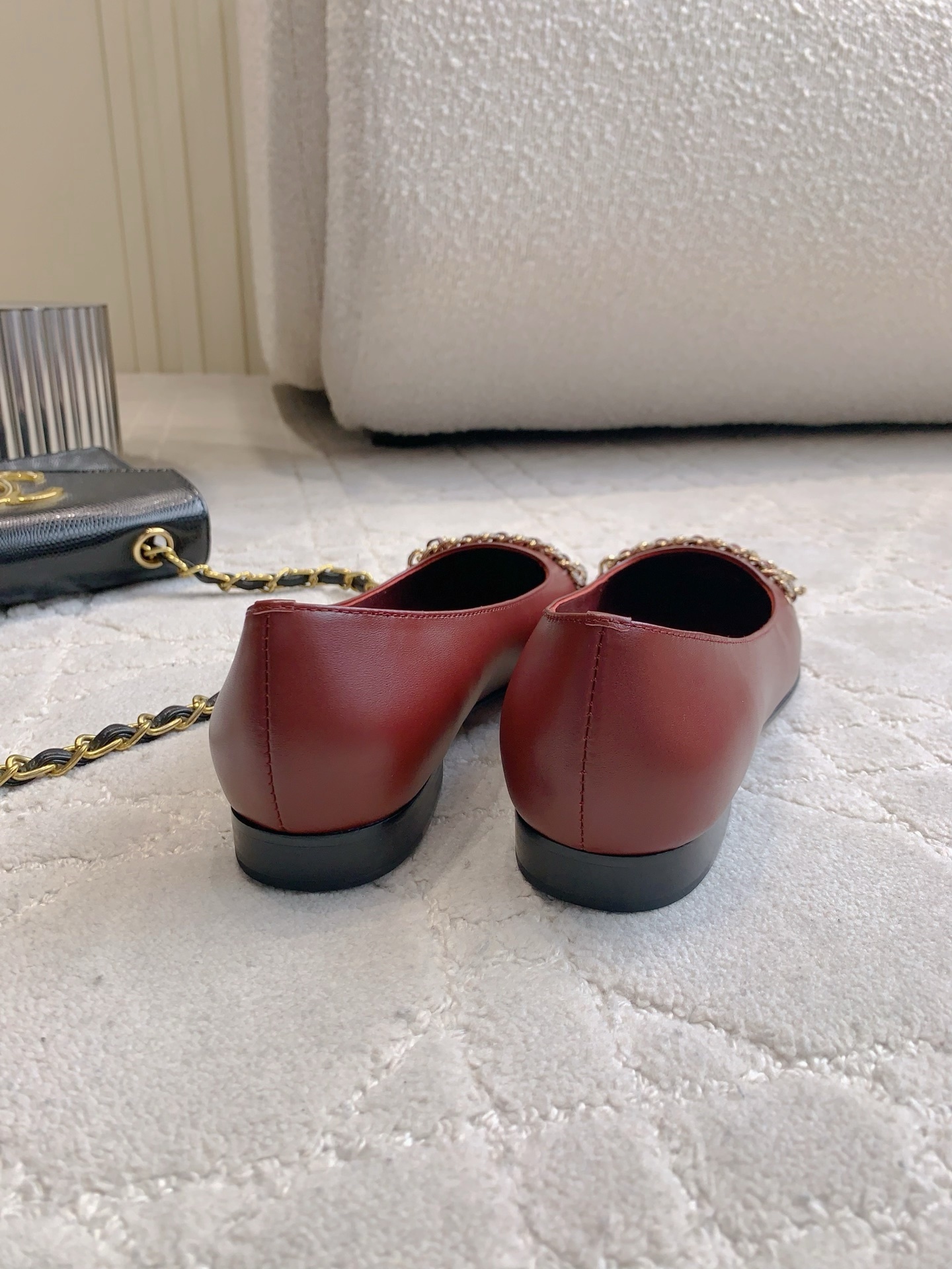 Luxury burgundy red Chanel leather ballet flats with gold chain and CC logo detail on a marble table. - Hình 5