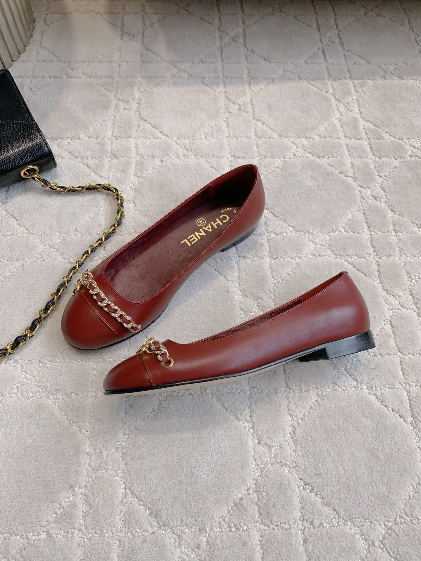 Luxury burgundy red Chanel leather ballet flats with gold chain and CC logo detail on a marble table. - Hình 4
