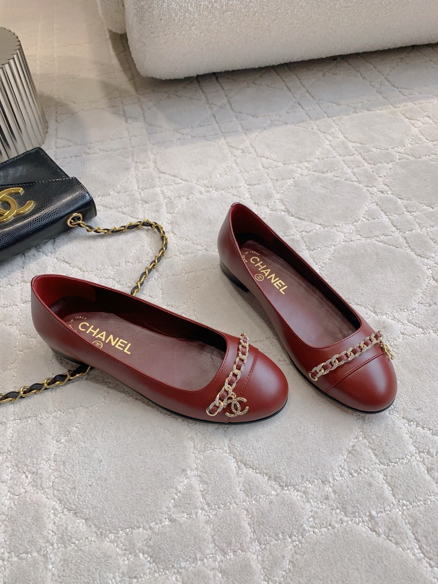 Luxury burgundy red Chanel leather ballet flats with gold chain and CC logo detail on a marble table. - Hình 3