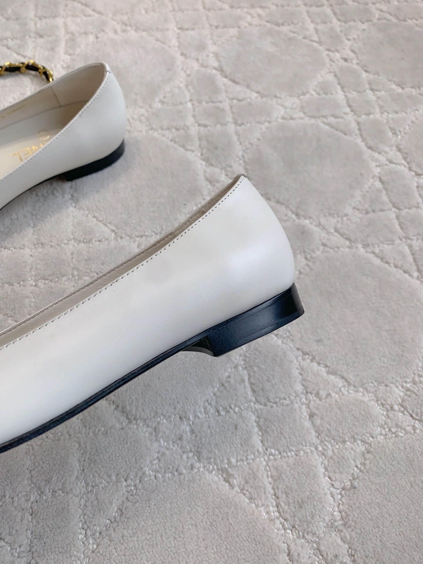 A pair of luxury Chanel white leather ballerina flats with gold chain and CC logo charm on a white marble table. - Hình 9