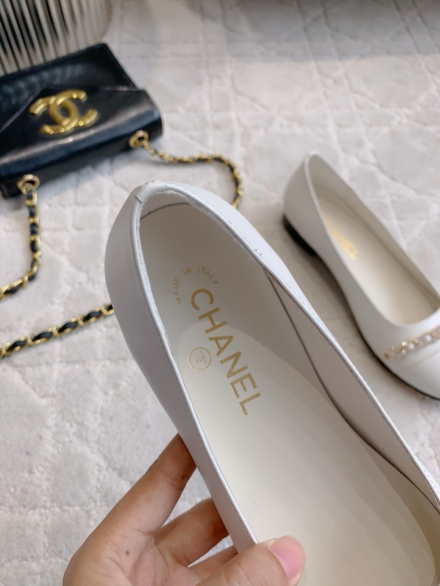 A pair of luxury Chanel white leather ballerina flats with gold chain and CC logo charm on a white marble table. - Hình 8