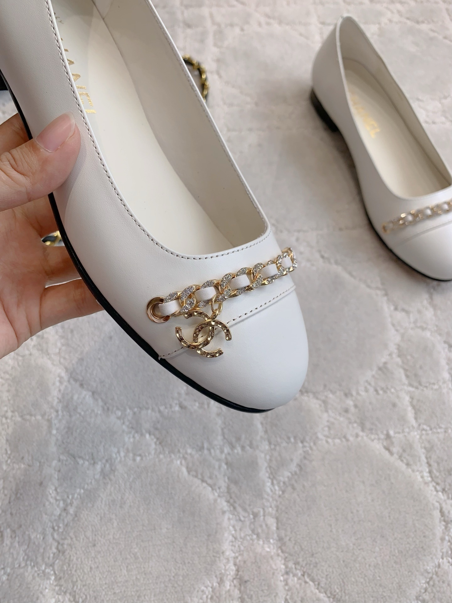 A pair of luxury Chanel white leather ballerina flats with gold chain and CC logo charm on a white marble table. - Hình 7