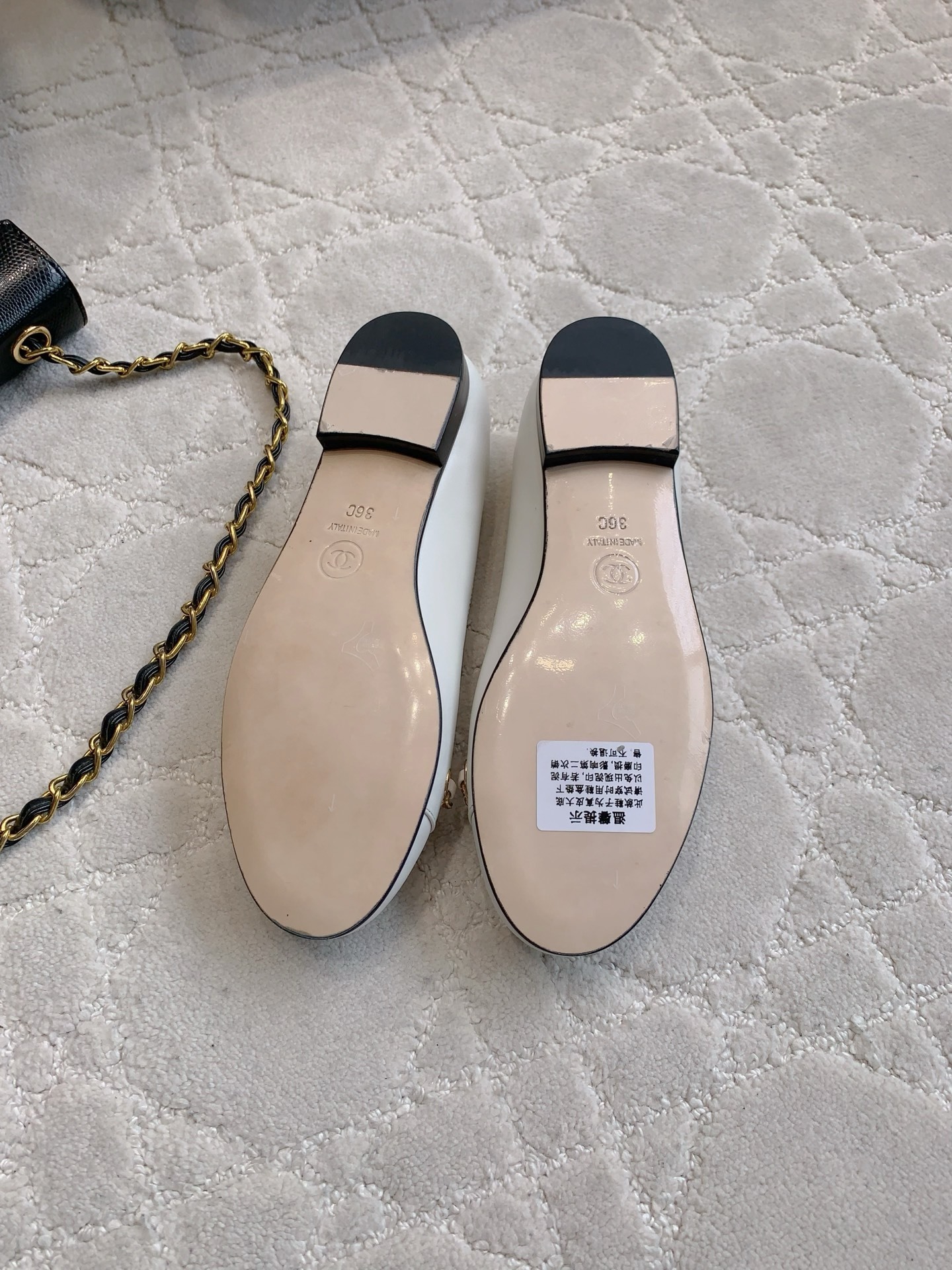 A pair of luxury Chanel white leather ballerina flats with gold chain and CC logo charm on a white marble table. - Hình 6