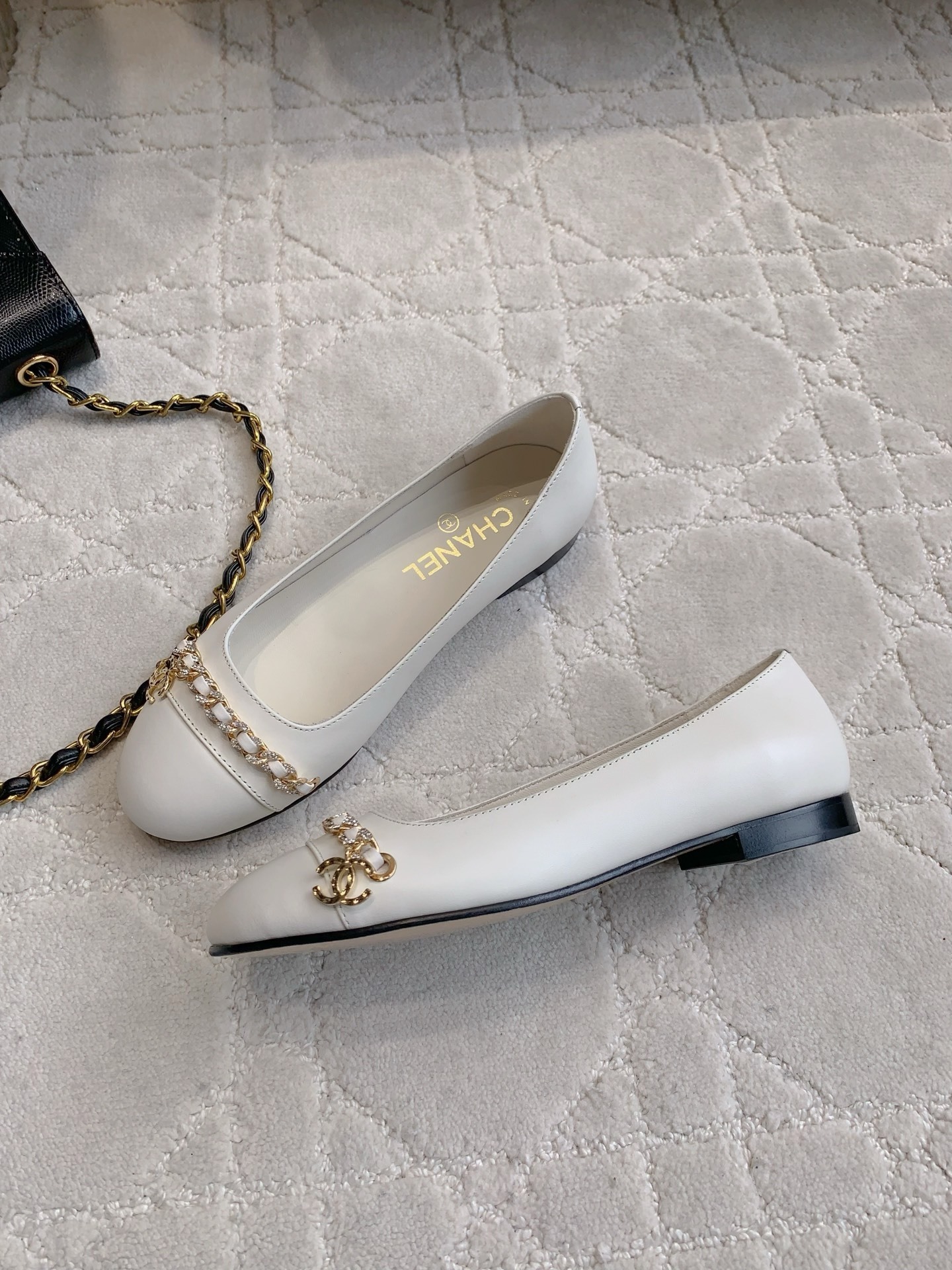 A pair of luxury Chanel white leather ballerina flats with gold chain and CC logo charm on a white marble table. - Hình 4