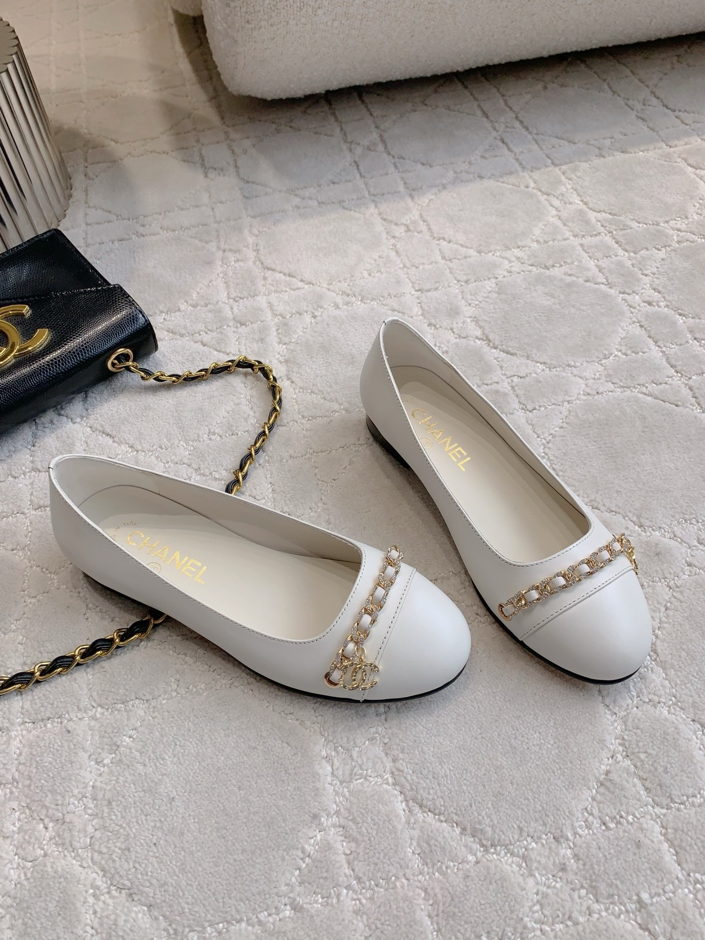 A pair of luxury Chanel white leather ballerina flats with gold chain and CC logo charm on a white marble table. - Hình 3