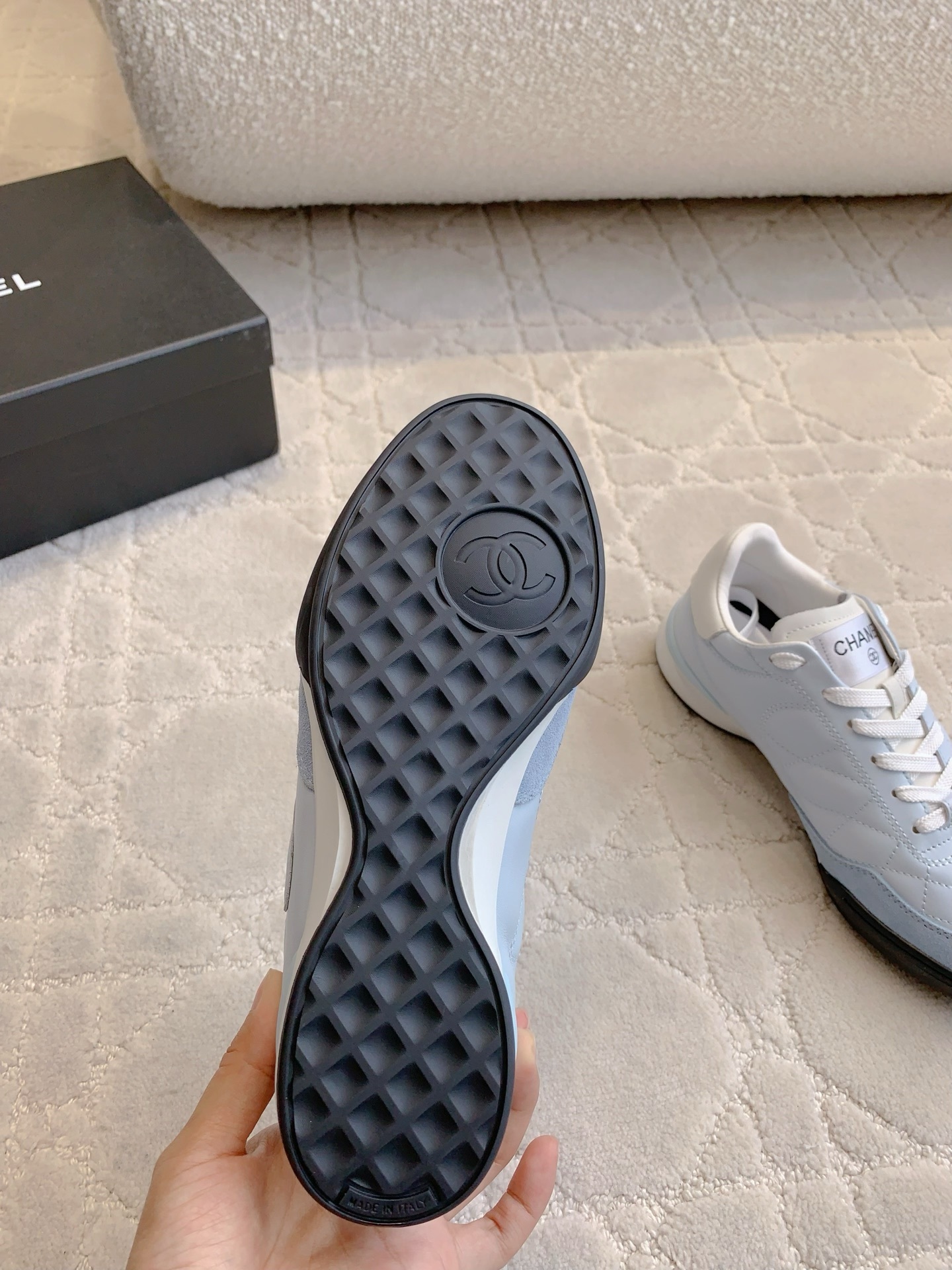 A pair of Chanel light blue quilted leather sneakers with white laces and interlocking CC logo on a neutral textured background - Hình 9