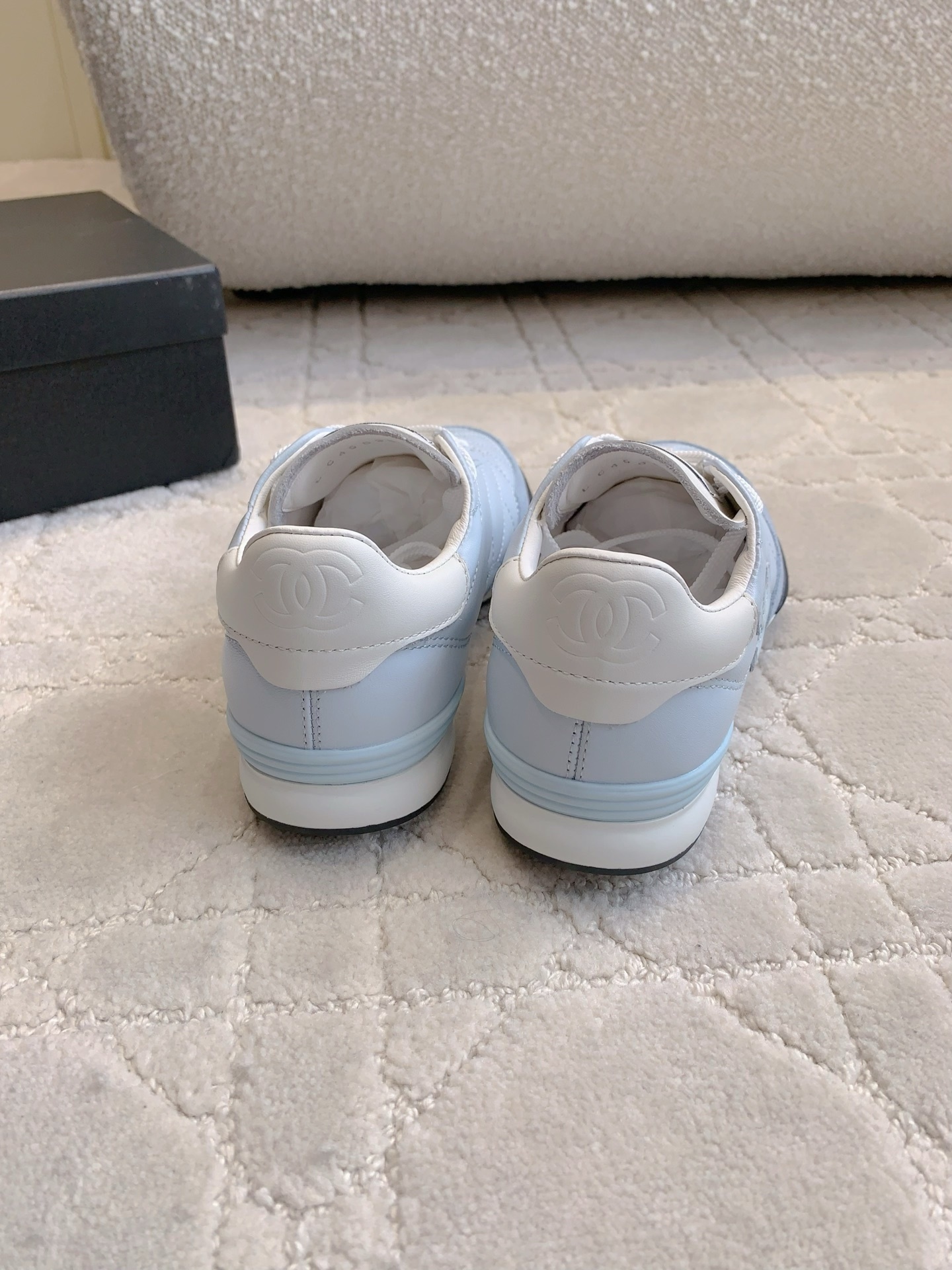 A pair of Chanel light blue quilted leather sneakers with white laces and interlocking CC logo on a neutral textured background - Hình 8