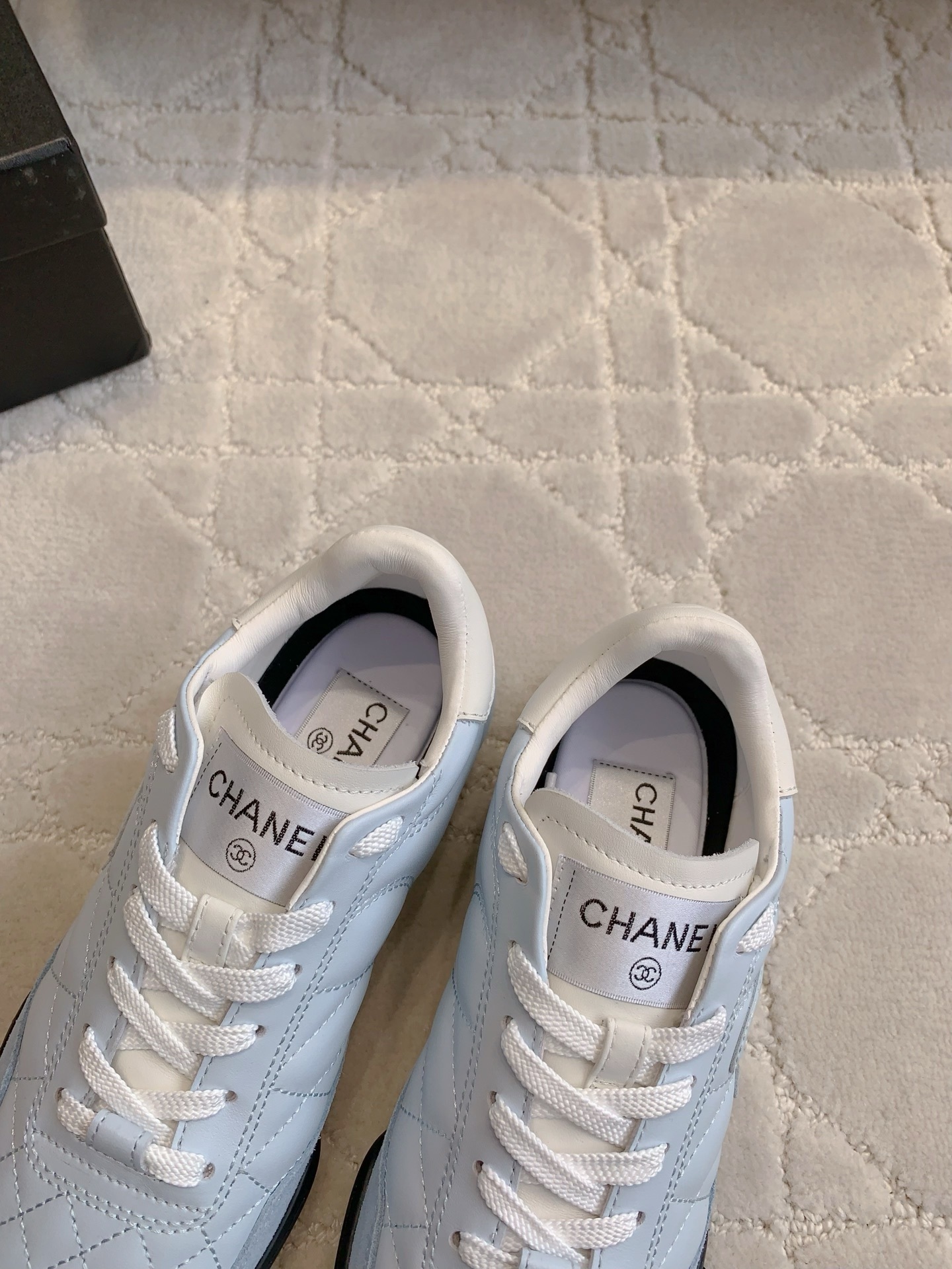 A pair of Chanel light blue quilted leather sneakers with white laces and interlocking CC logo on a neutral textured background - Hình 7