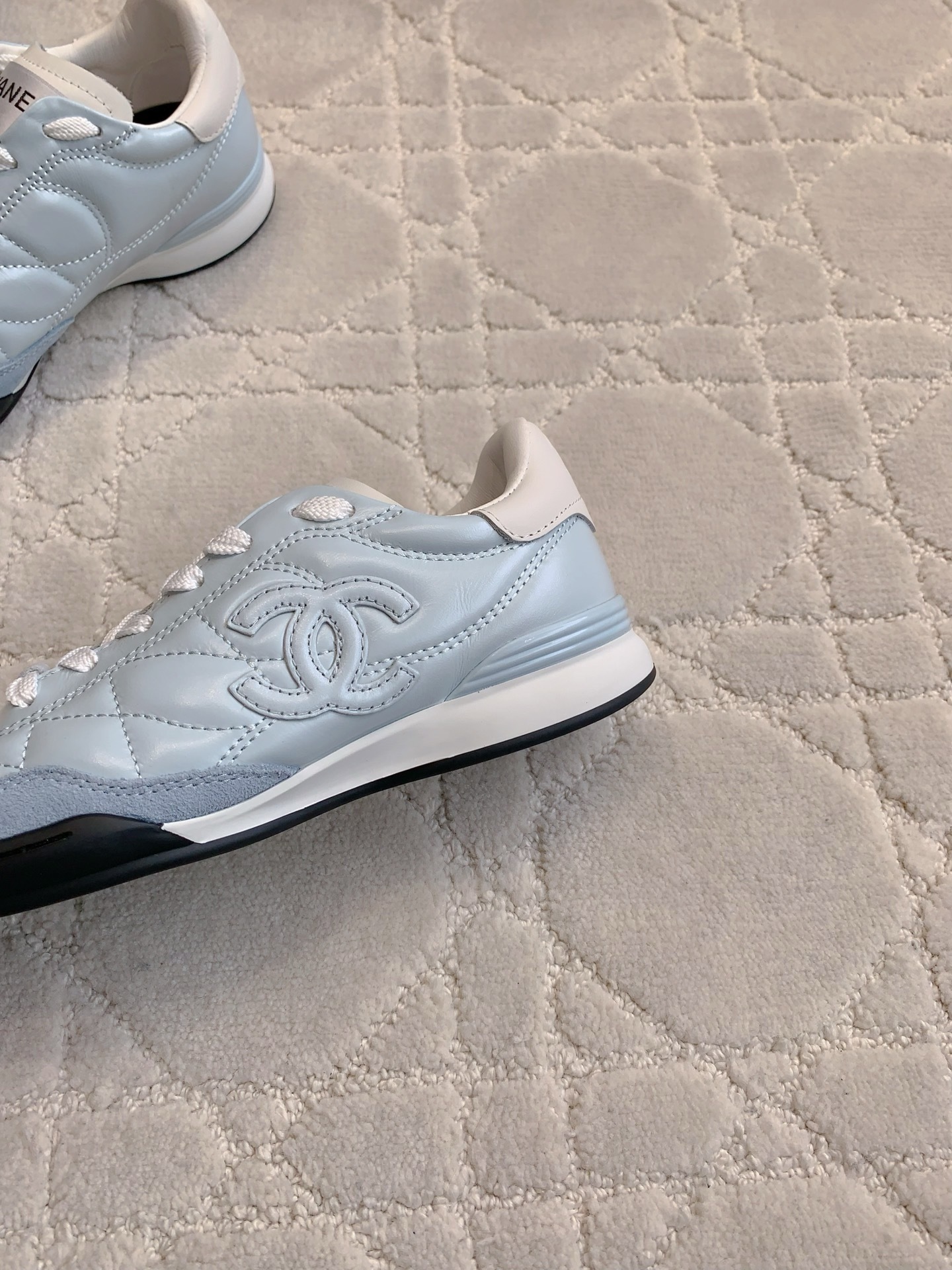 A pair of Chanel light blue quilted leather sneakers with white laces and interlocking CC logo on a neutral textured background - Hình 6