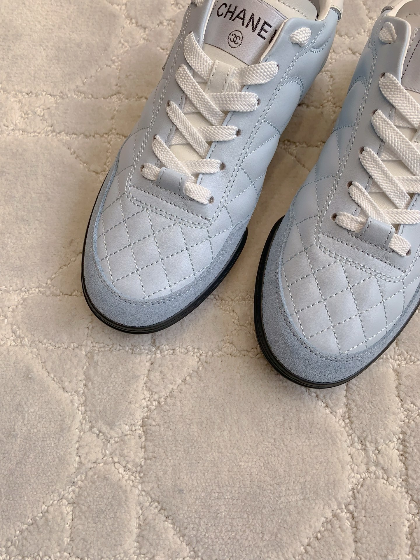 A pair of Chanel light blue quilted leather sneakers with white laces and interlocking CC logo on a neutral textured background - Hình 5
