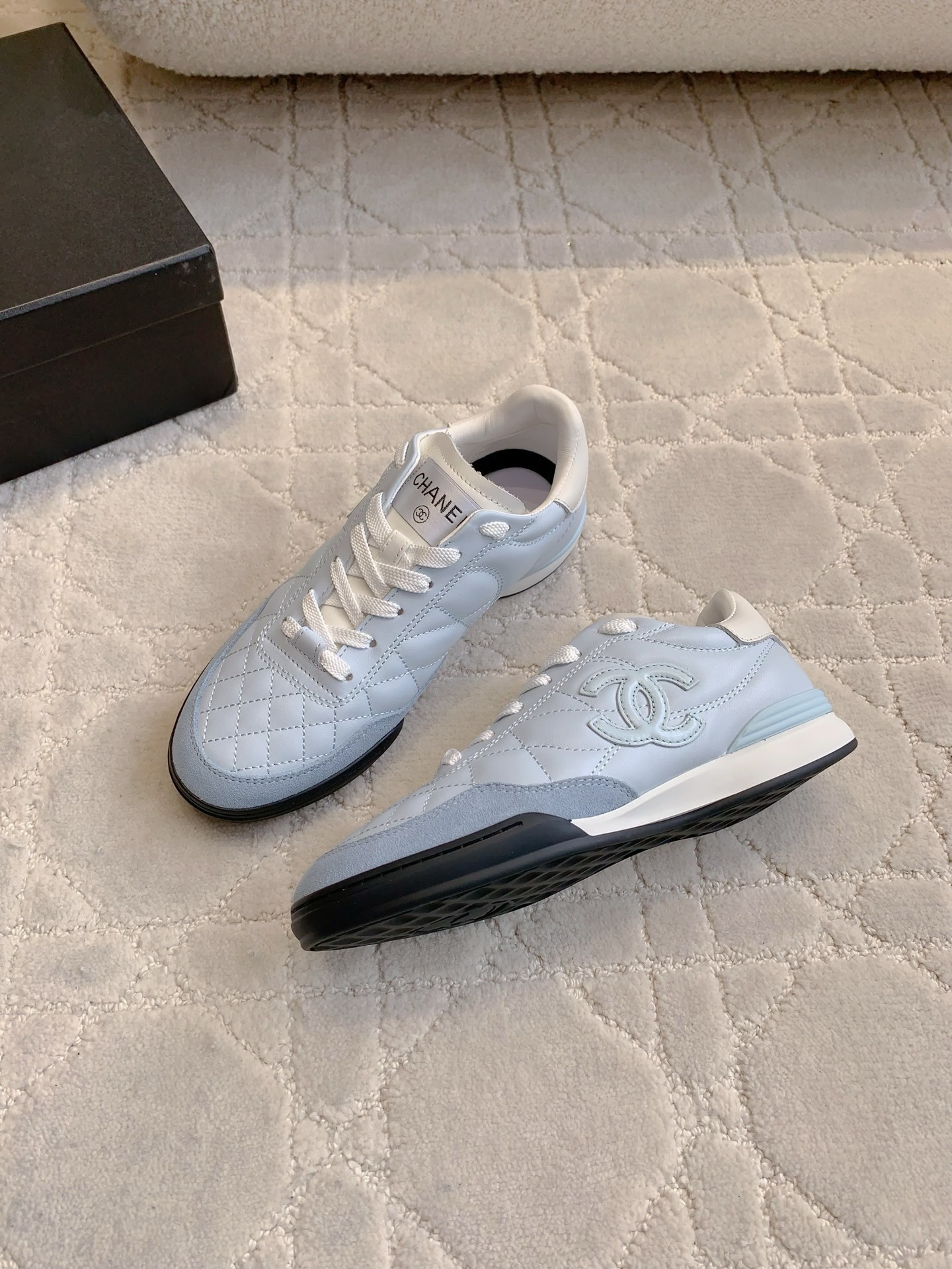 A pair of Chanel light blue quilted leather sneakers with white laces and interlocking CC logo on a neutral textured background - Hình 4