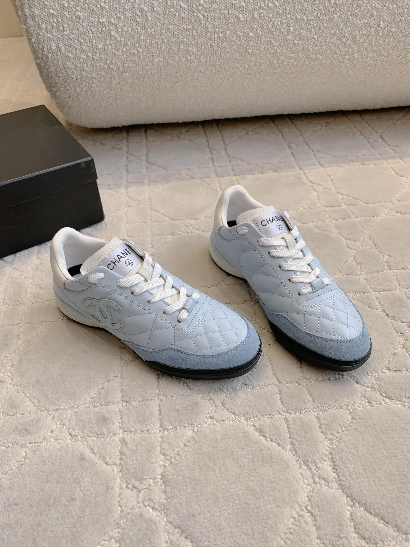 A pair of Chanel light blue quilted leather sneakers with white laces and interlocking CC logo on a neutral textured background - Hình 3