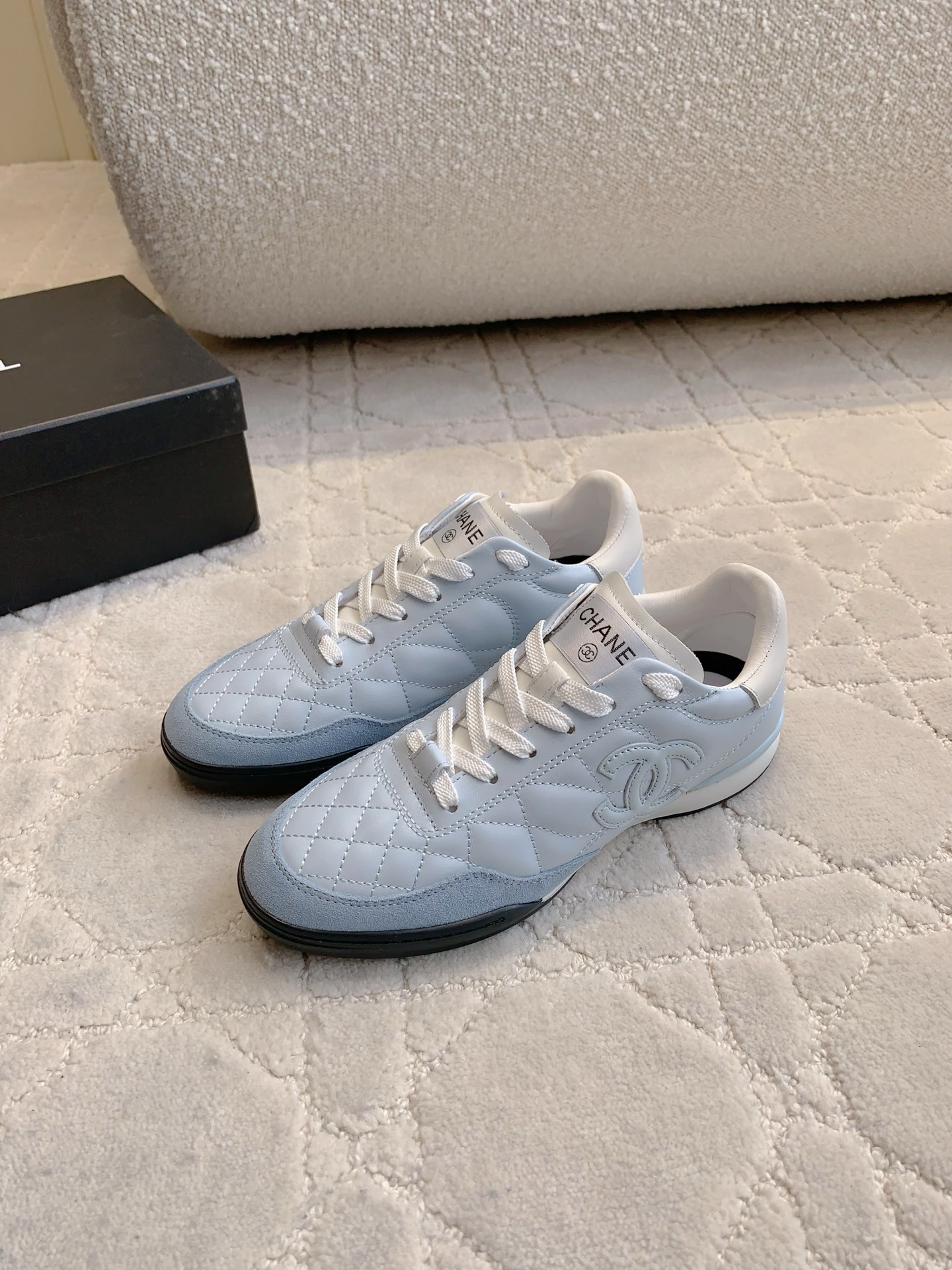 A pair of Chanel light blue quilted leather sneakers with white laces and interlocking CC logo on a neutral textured background - Hình 2