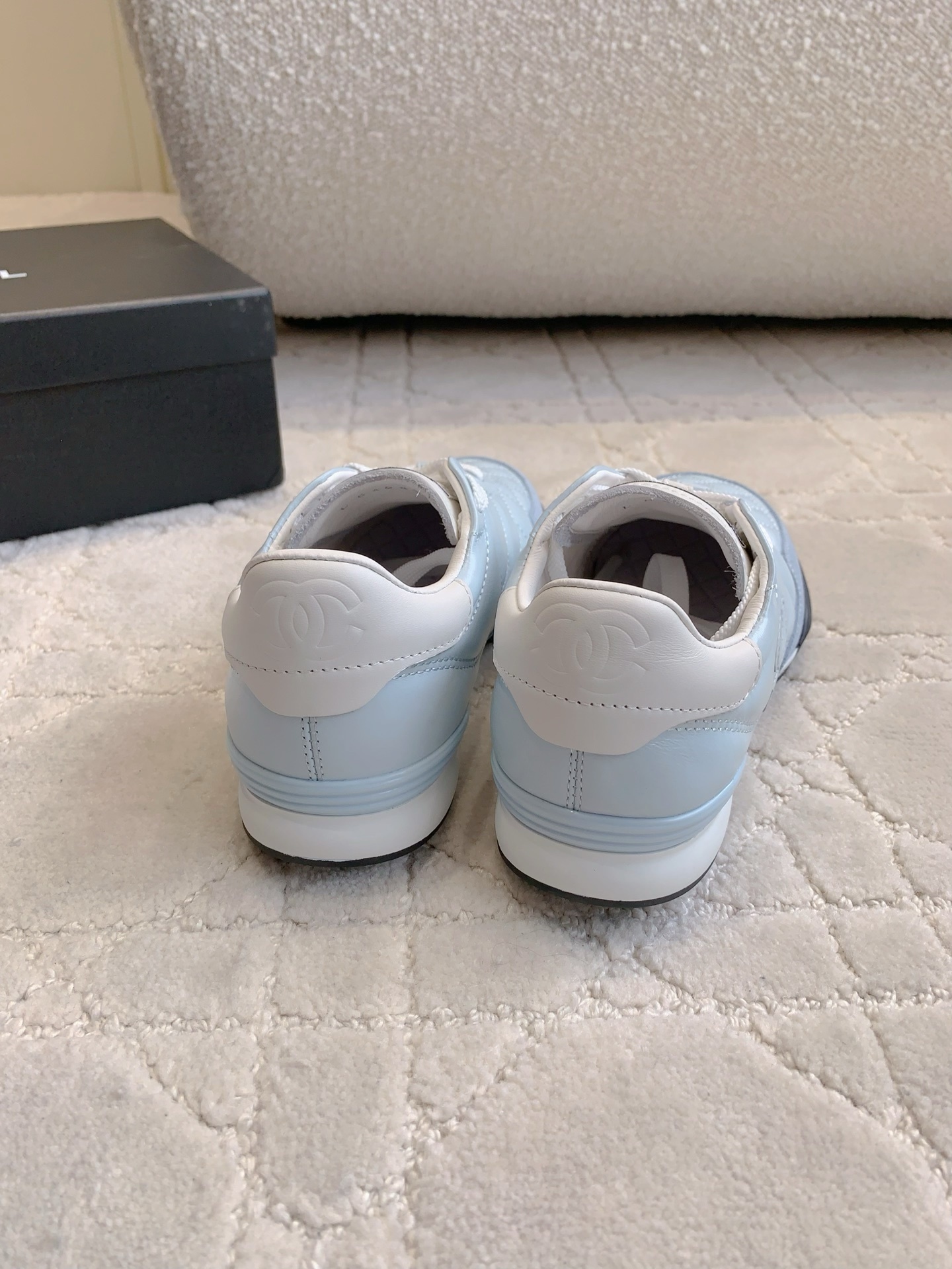 A pair of light blue Chanel quilted leather sneakers with suede toe caps and white laces displayed on a patterned carpet. - Hình 8