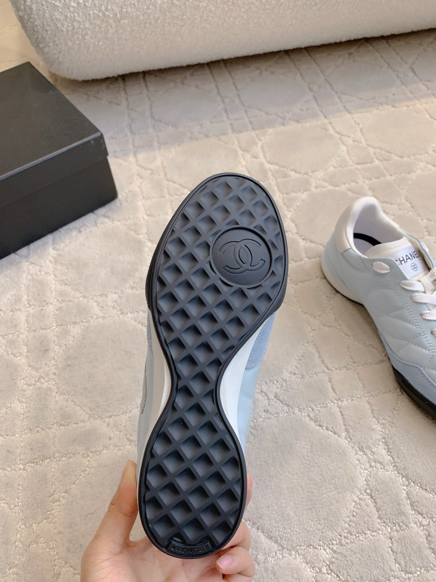 A pair of light blue Chanel quilted leather sneakers with suede toe caps and white laces displayed on a patterned carpet. - Hình 7