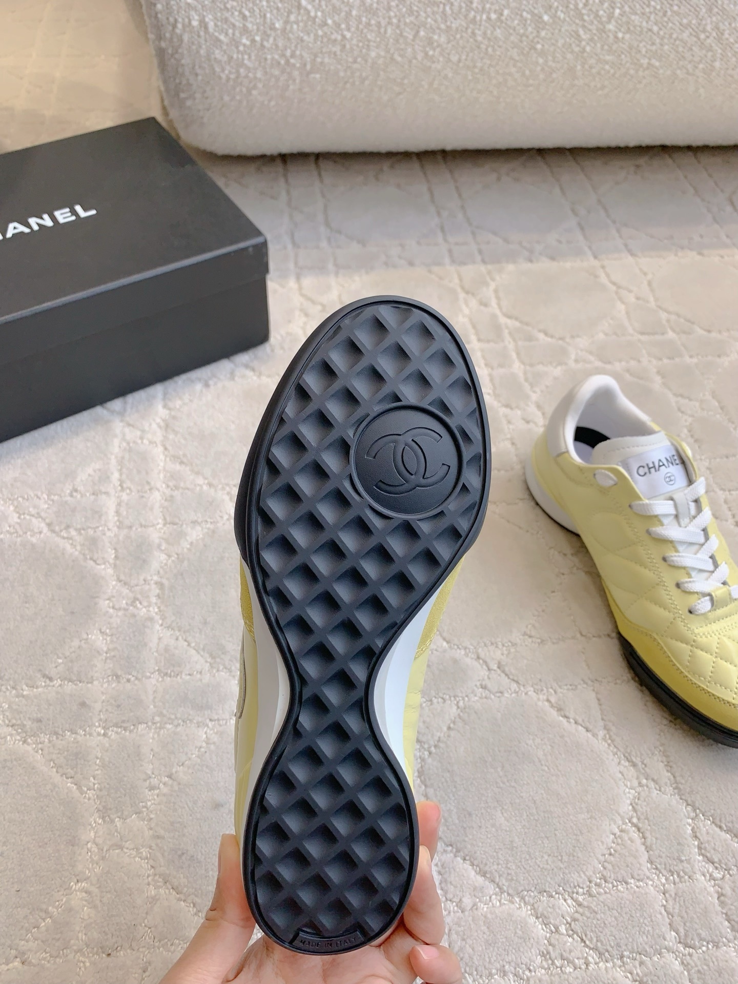 A pair of luxury pastel yellow Chanel sneakers with quilted leather and interlocking CC logo on a white textured rug. - Hình 9