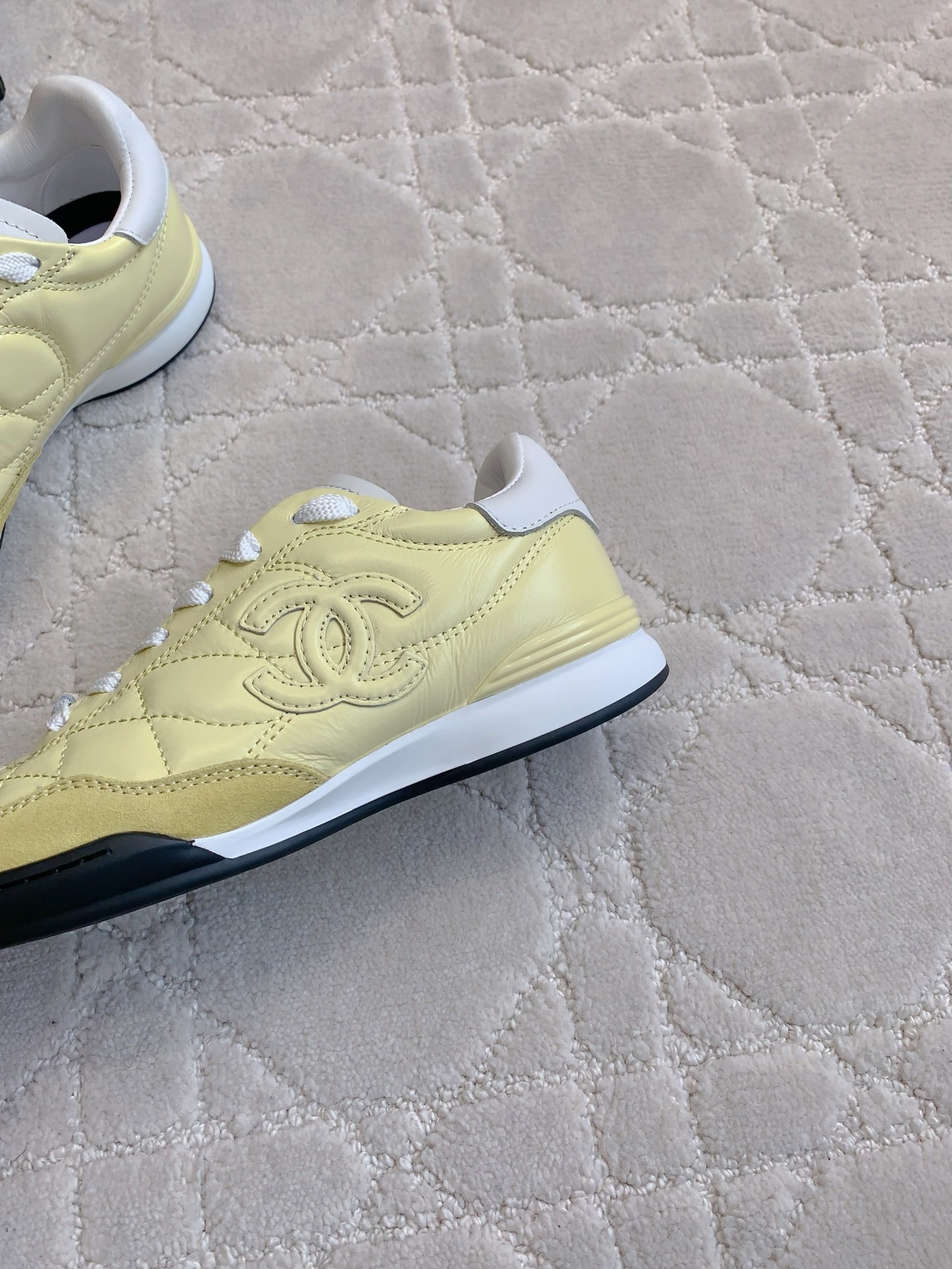 A pair of luxury pastel yellow Chanel sneakers with quilted leather and interlocking CC logo on a white textured rug. - Hình 7