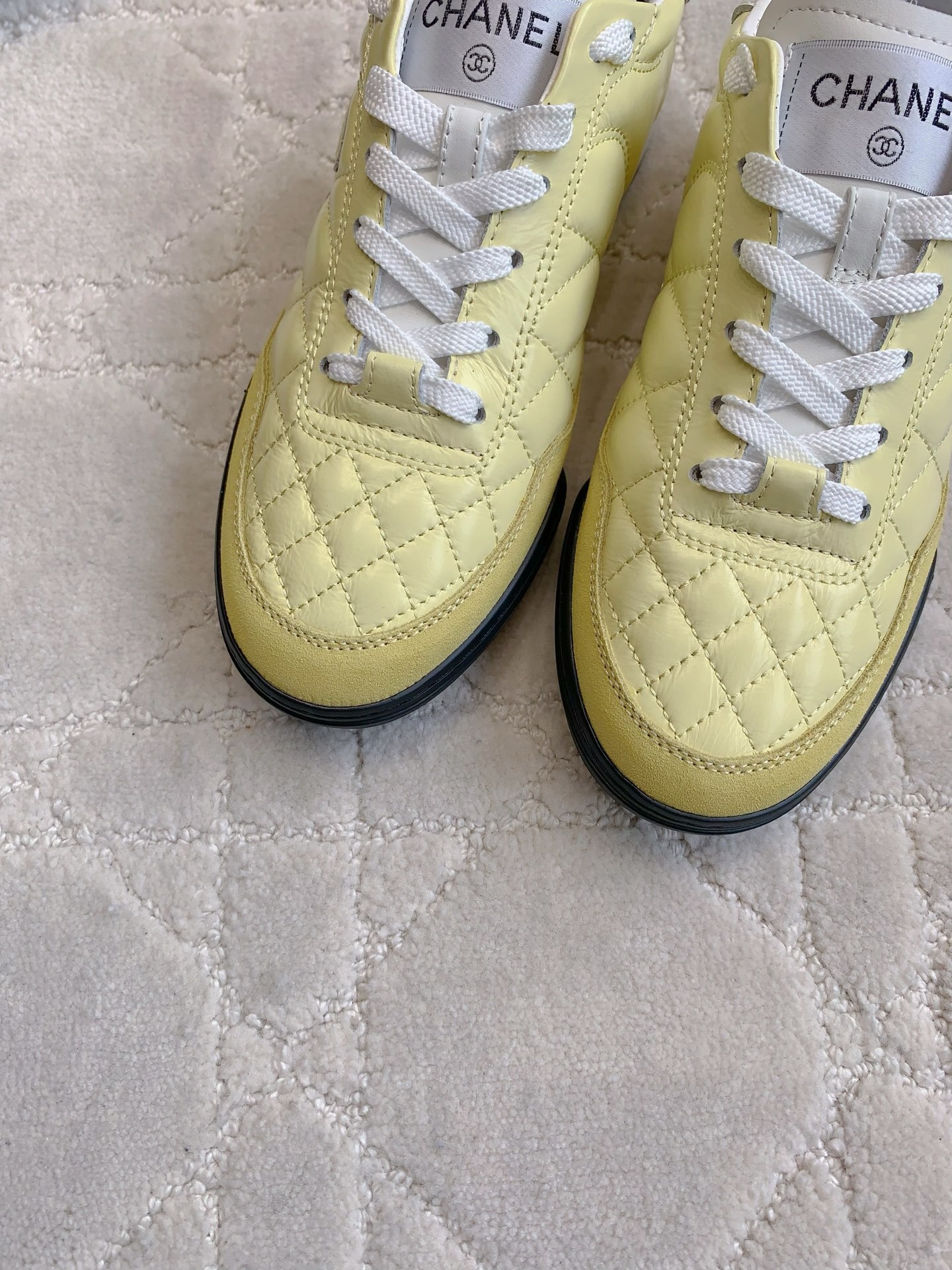 A pair of luxury pastel yellow Chanel sneakers with quilted leather and interlocking CC logo on a white textured rug. - Hình 5