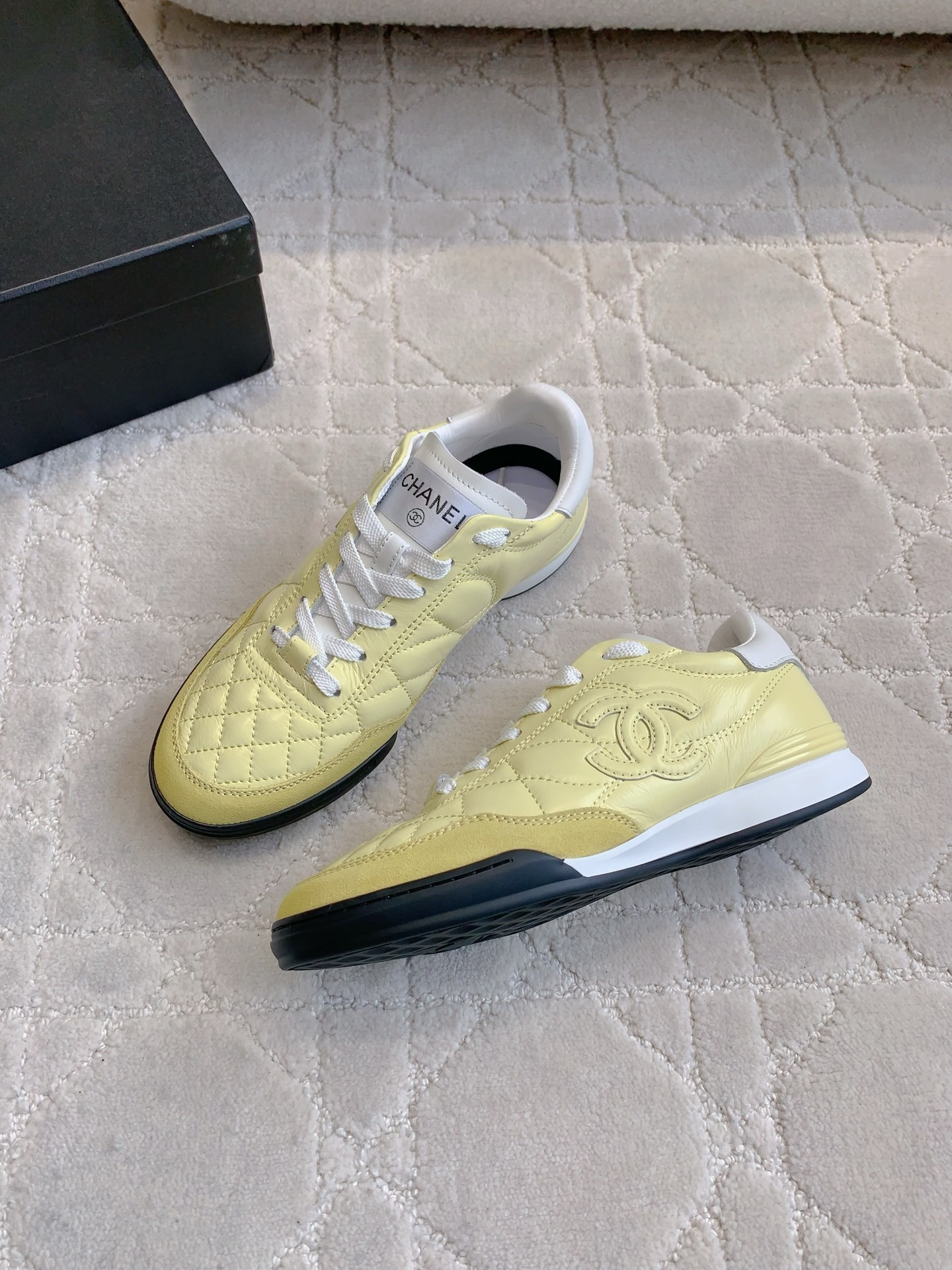 A pair of luxury pastel yellow Chanel sneakers with quilted leather and interlocking CC logo on a white textured rug. - Hình 4