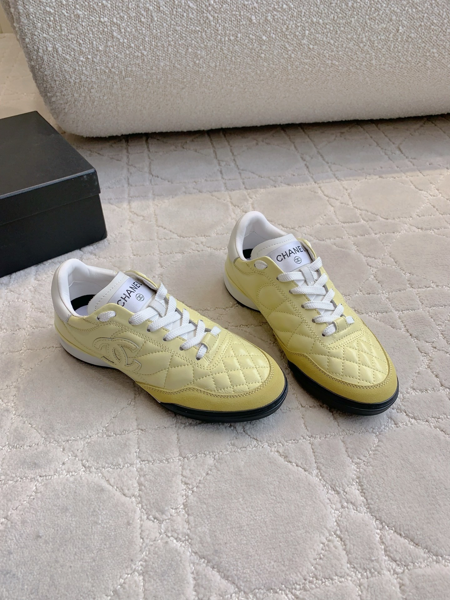 A pair of luxury pastel yellow Chanel sneakers with quilted leather and interlocking CC logo on a white textured rug. - Hình 3