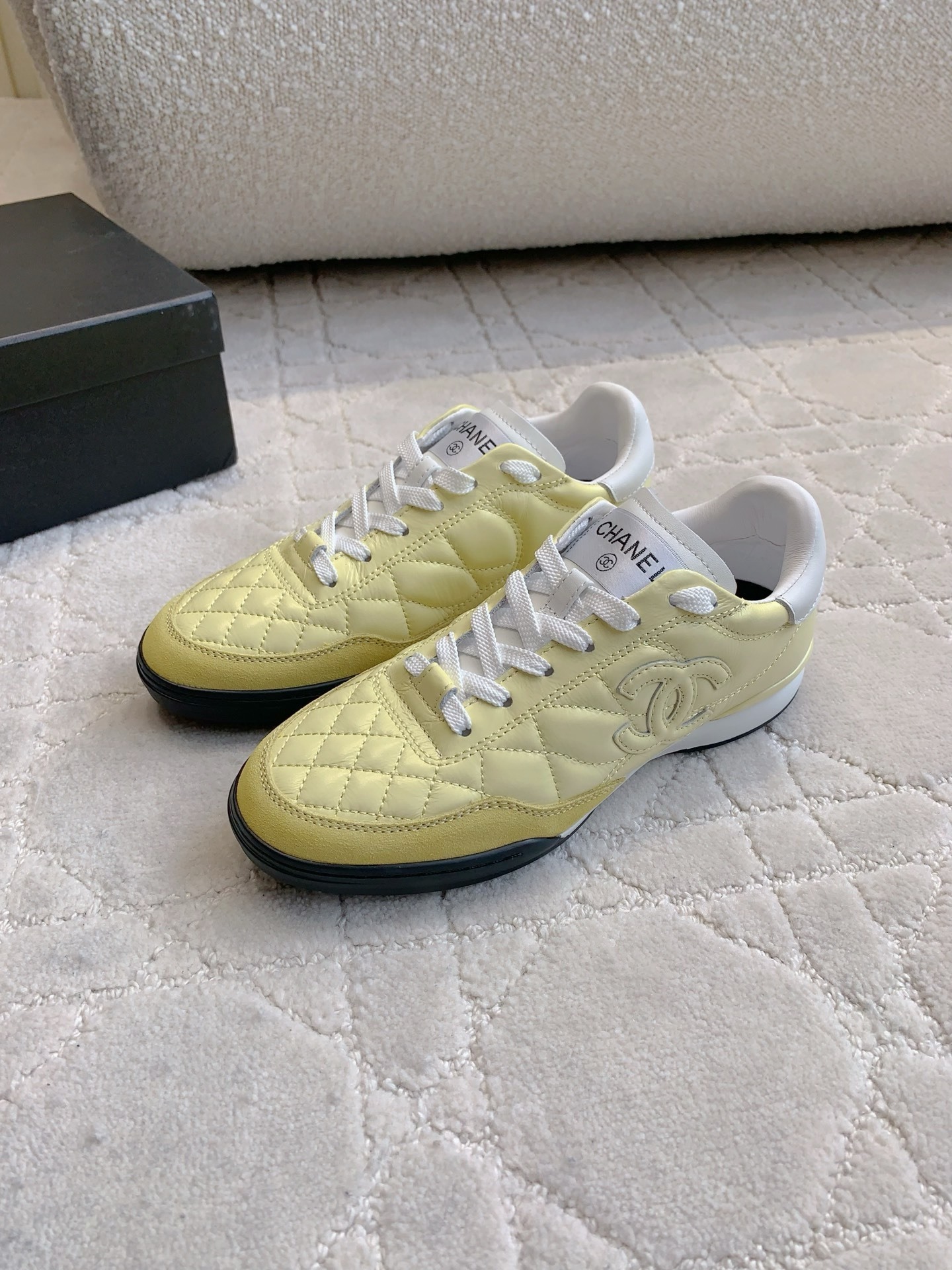 A pair of luxury pastel yellow Chanel sneakers with quilted leather and interlocking CC logo on a white textured rug. - Hình 2