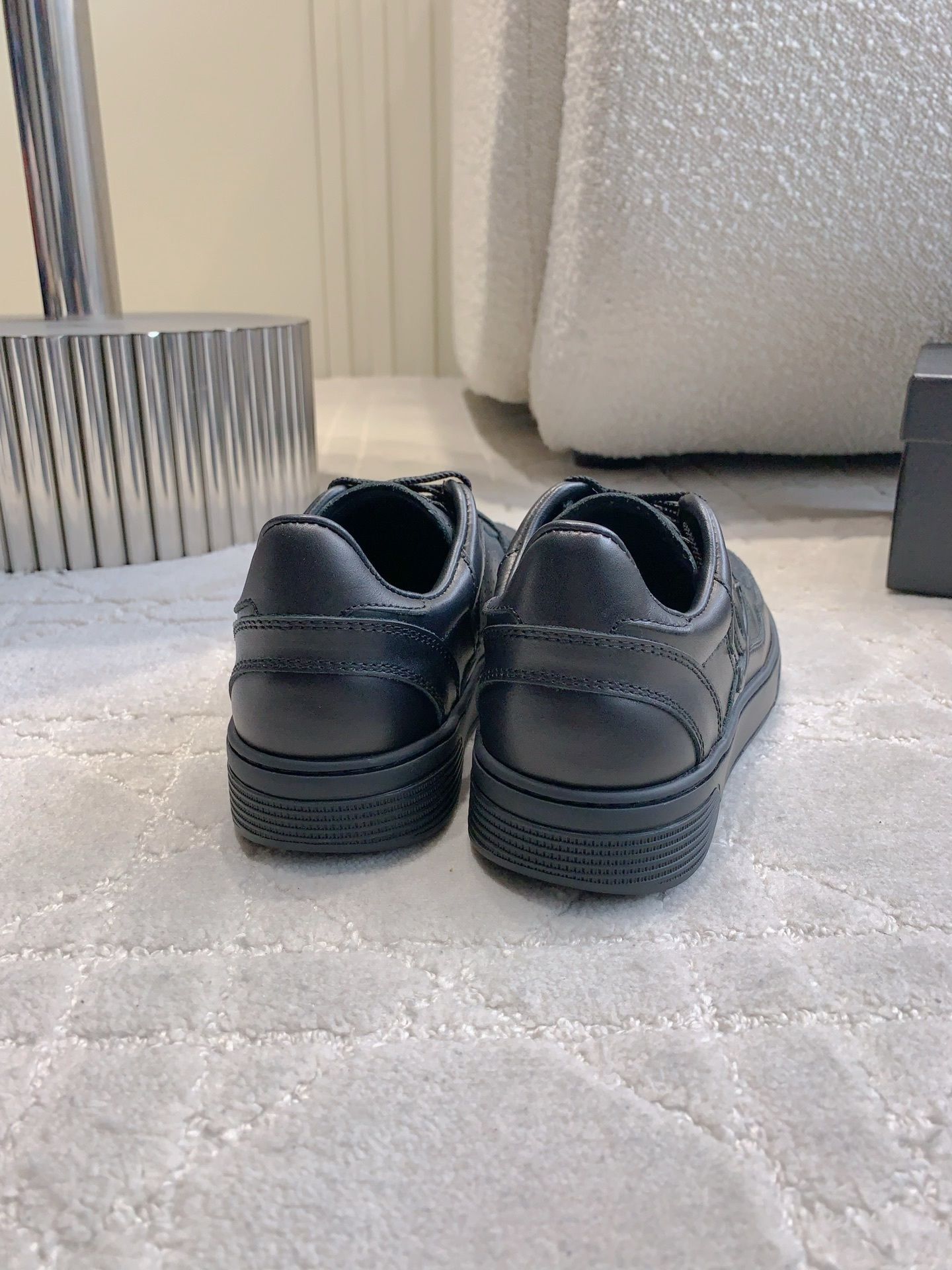 A pair of black Chanel leather sneakers featuring the interlocking CC logo and perforated details on a white textured carpet. - Hình 8