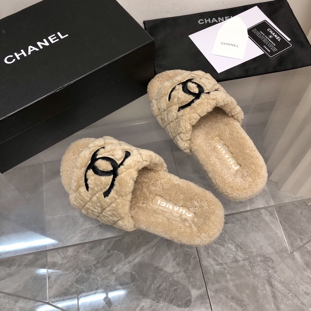 A pair of beige Chanel shearling quilted slides with a black CC logo displayed on a marble floor with its original box and dust bag. - Hình 9