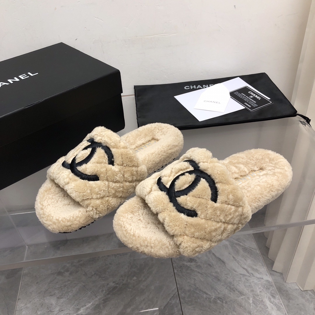A pair of beige Chanel shearling quilted slides with a black CC logo displayed on a marble floor with its original box and dust bag. - Hình 8