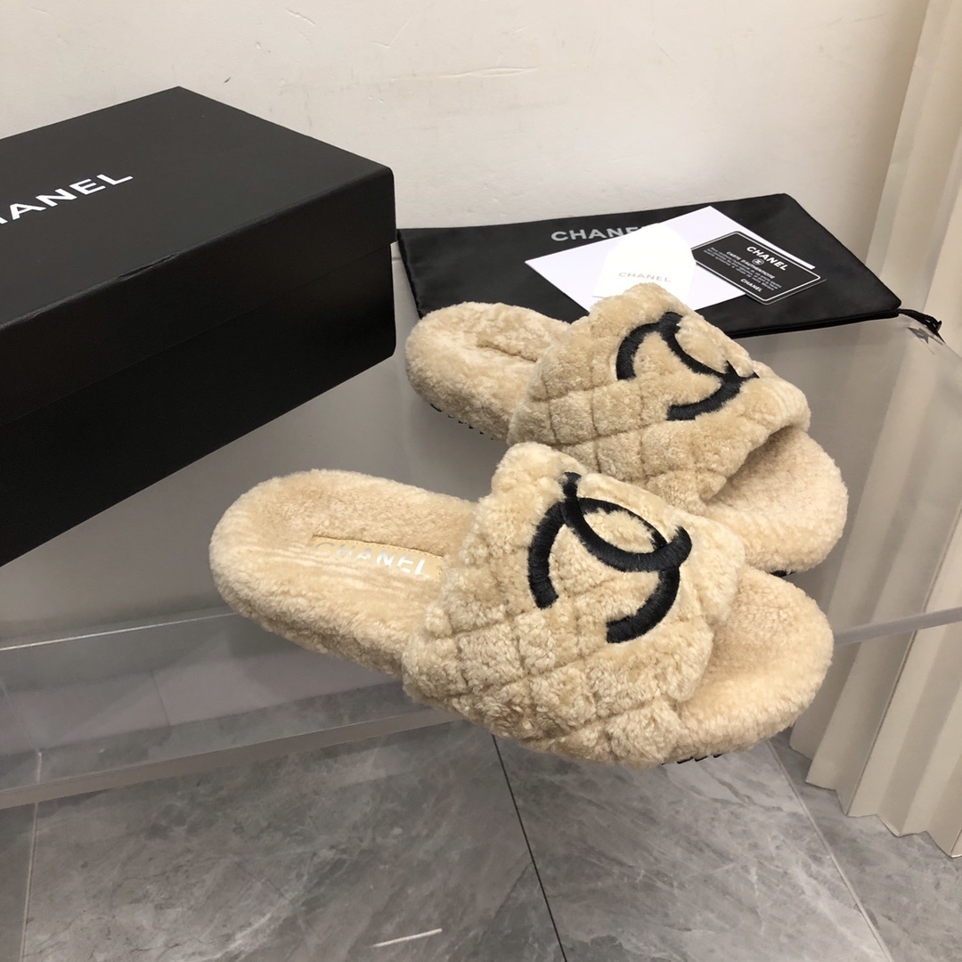 A pair of beige Chanel shearling quilted slides with a black CC logo displayed on a marble floor with its original box and dust bag. - Hình 7