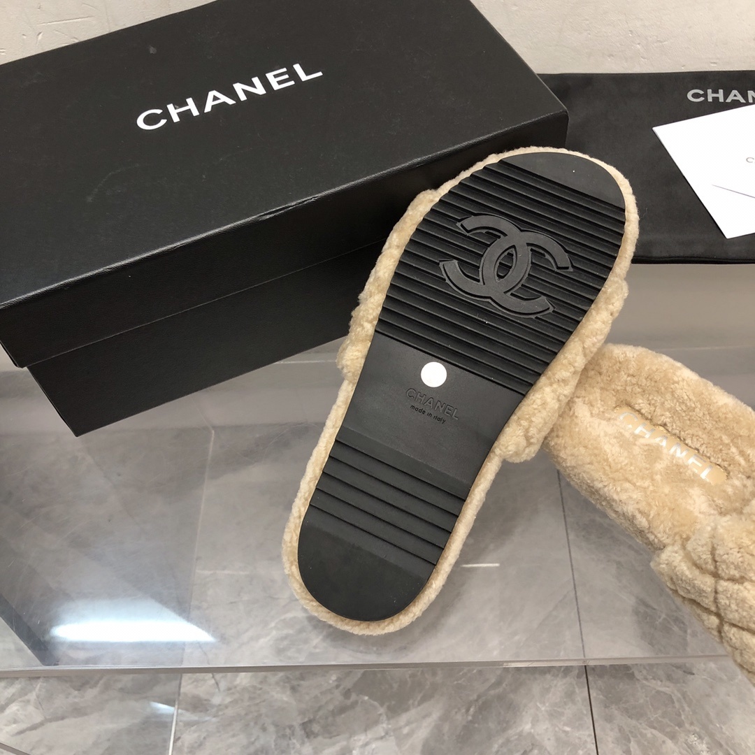 A pair of beige Chanel shearling quilted slides with a black CC logo displayed on a marble floor with its original box and dust bag. - Hình 6