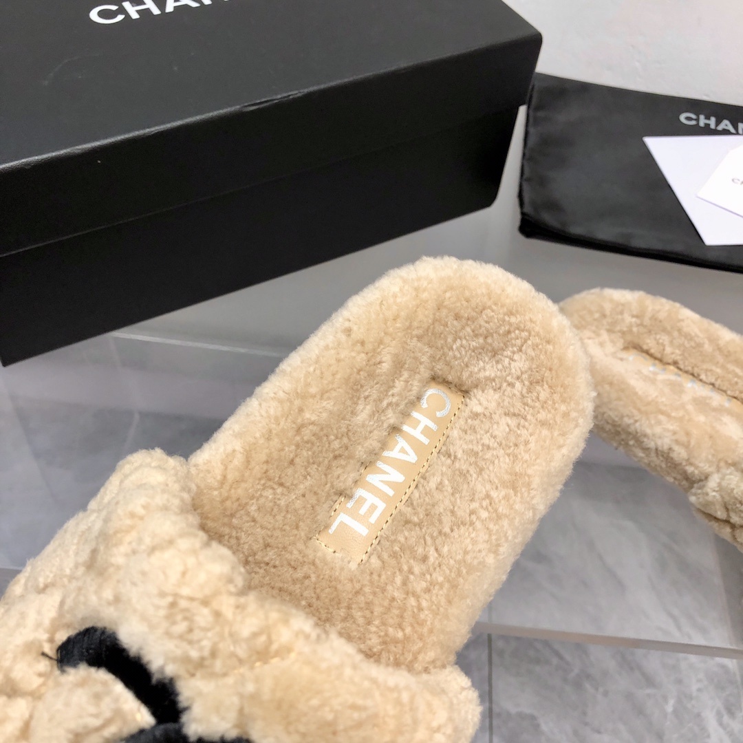 A pair of beige Chanel shearling quilted slides with a black CC logo displayed on a marble floor with its original box and dust bag. - Hình 5