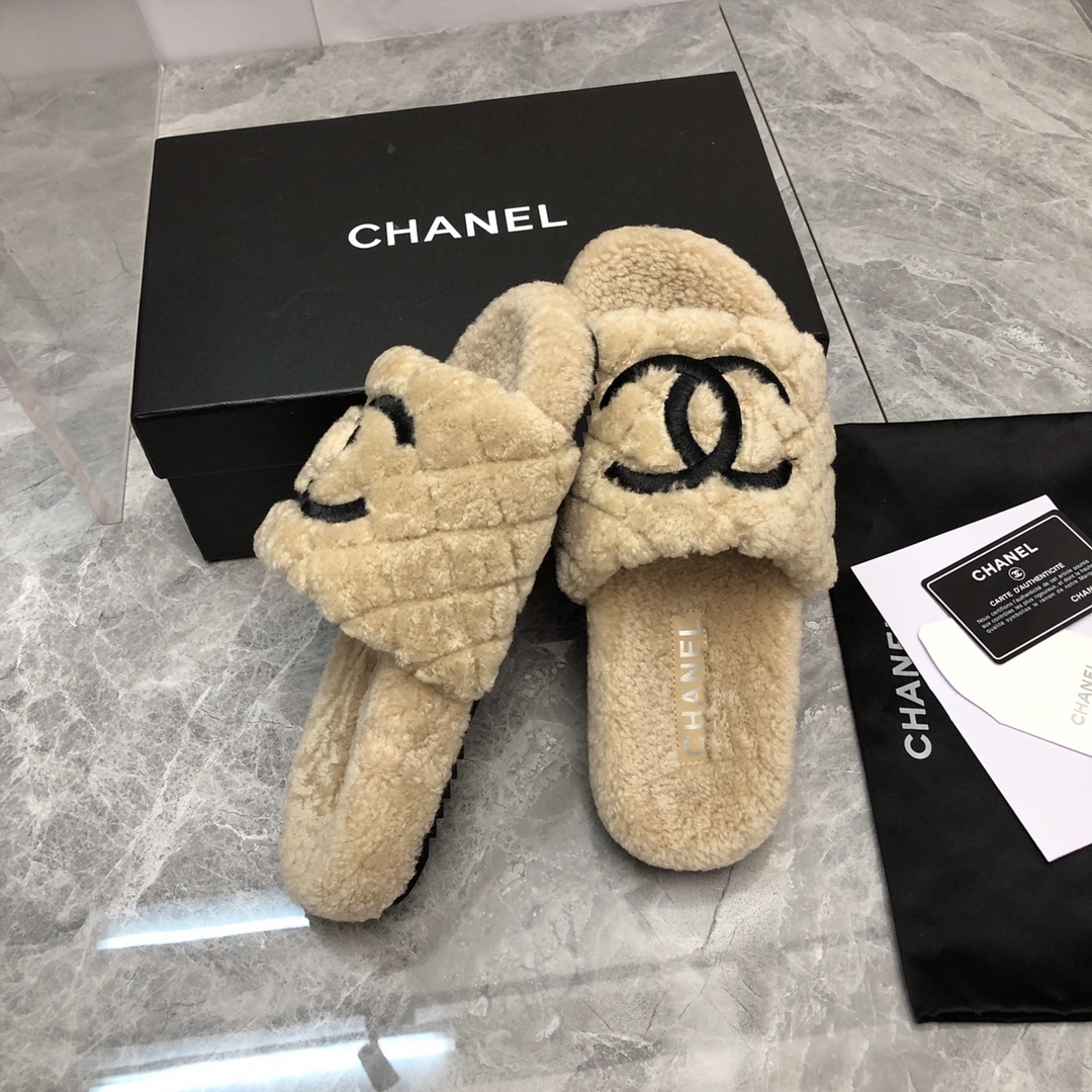 A pair of beige Chanel shearling quilted slides with a black CC logo displayed on a marble floor with its original box and dust bag. - Hình 2
