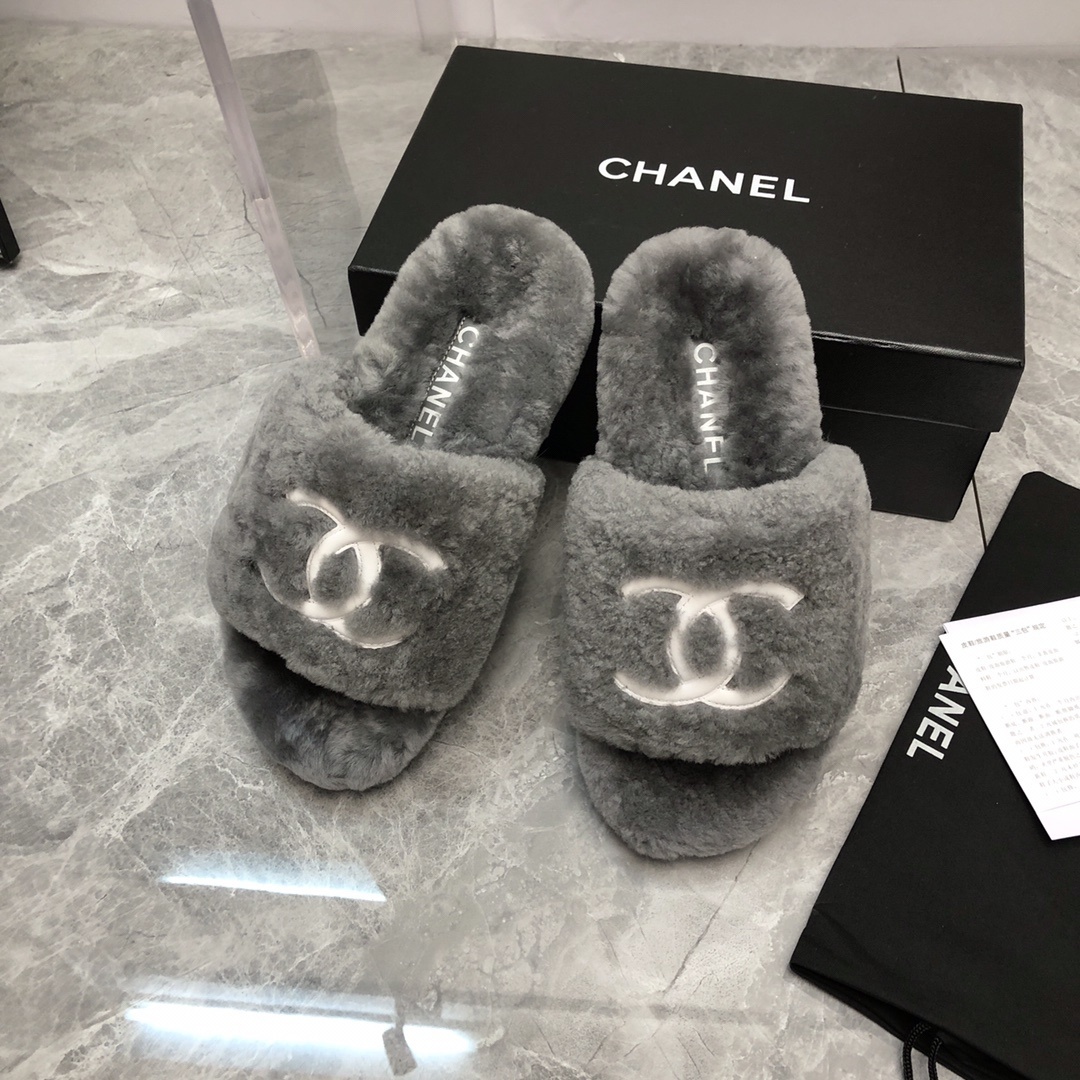 Pair of gray Chanel shearling fur slides with white CC logo on a glass table with original box and dust bag. - Hình 9