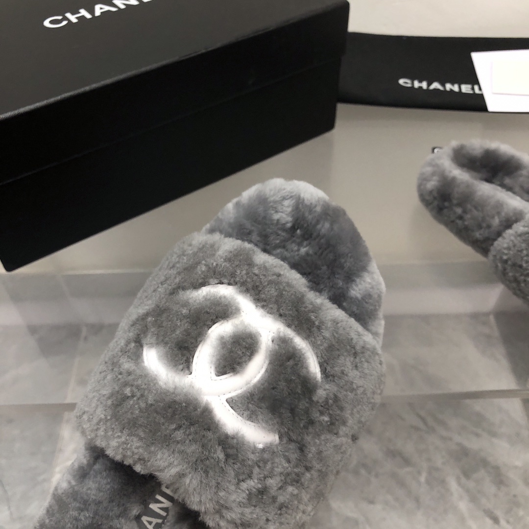 Pair of gray Chanel shearling fur slides with white CC logo on a glass table with original box and dust bag. - Hình 5