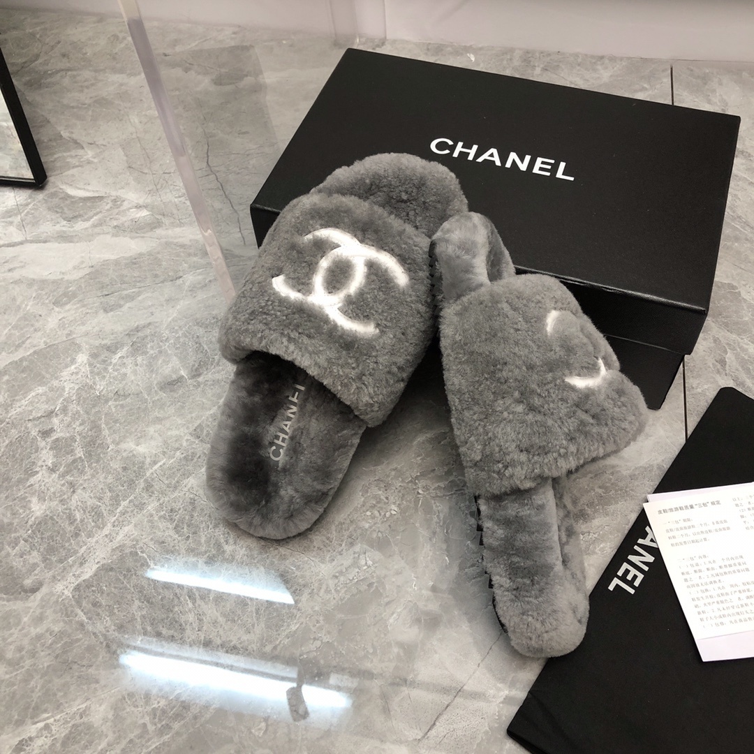 Pair of gray Chanel shearling fur slides with white CC logo on a glass table with original box and dust bag. - Hình 4