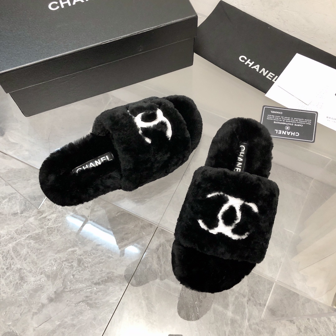 Pair of black fuzzy Chanel slippers with white interlocking CC logo on a glass table next to a designer box - Hình 8