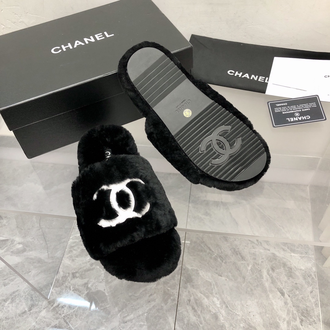 Pair of black fuzzy Chanel slippers with white interlocking CC logo on a glass table next to a designer box - Hình 7