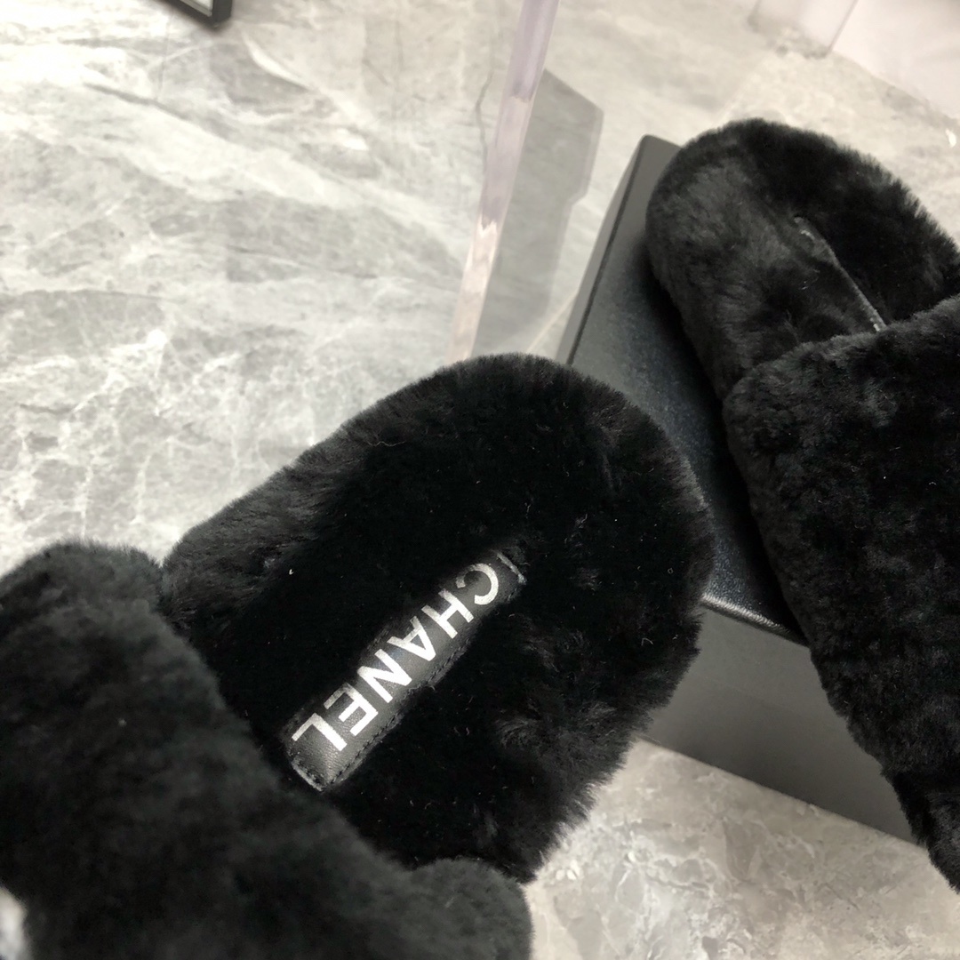 Pair of black fuzzy Chanel slippers with white interlocking CC logo on a glass table next to a designer box - Hình 6