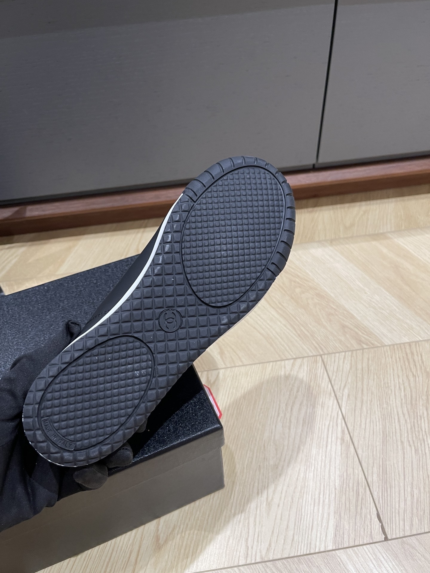 A pair of black Chanel low-top leather and suede sneakers with gold CC logos on the laces, sitting on a black Chanel shoe box. - Hình 9