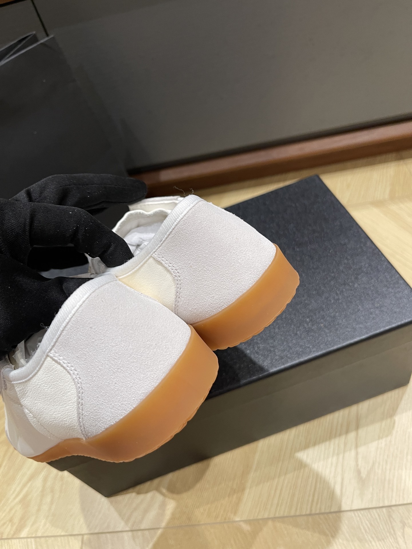 A pair of white Chanel low-top sneakers with suede trim and gum soles sitting on a black designer box next to a Chanel shopping bag. - Hình 8