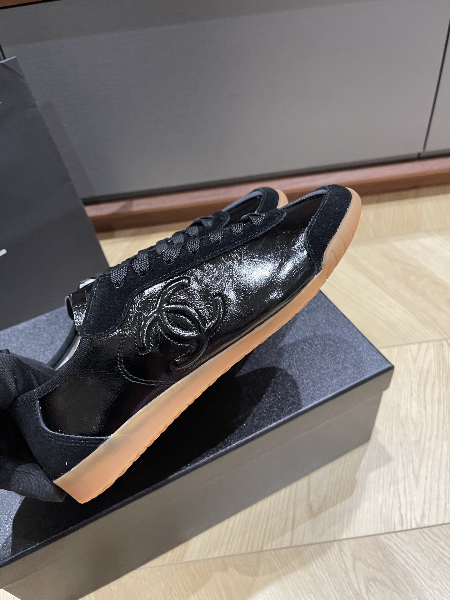 Pair of black Chanel sneakers in patent leather and suede with a gum sole, featuring the interlocking CC logo on the side. - Hình 5