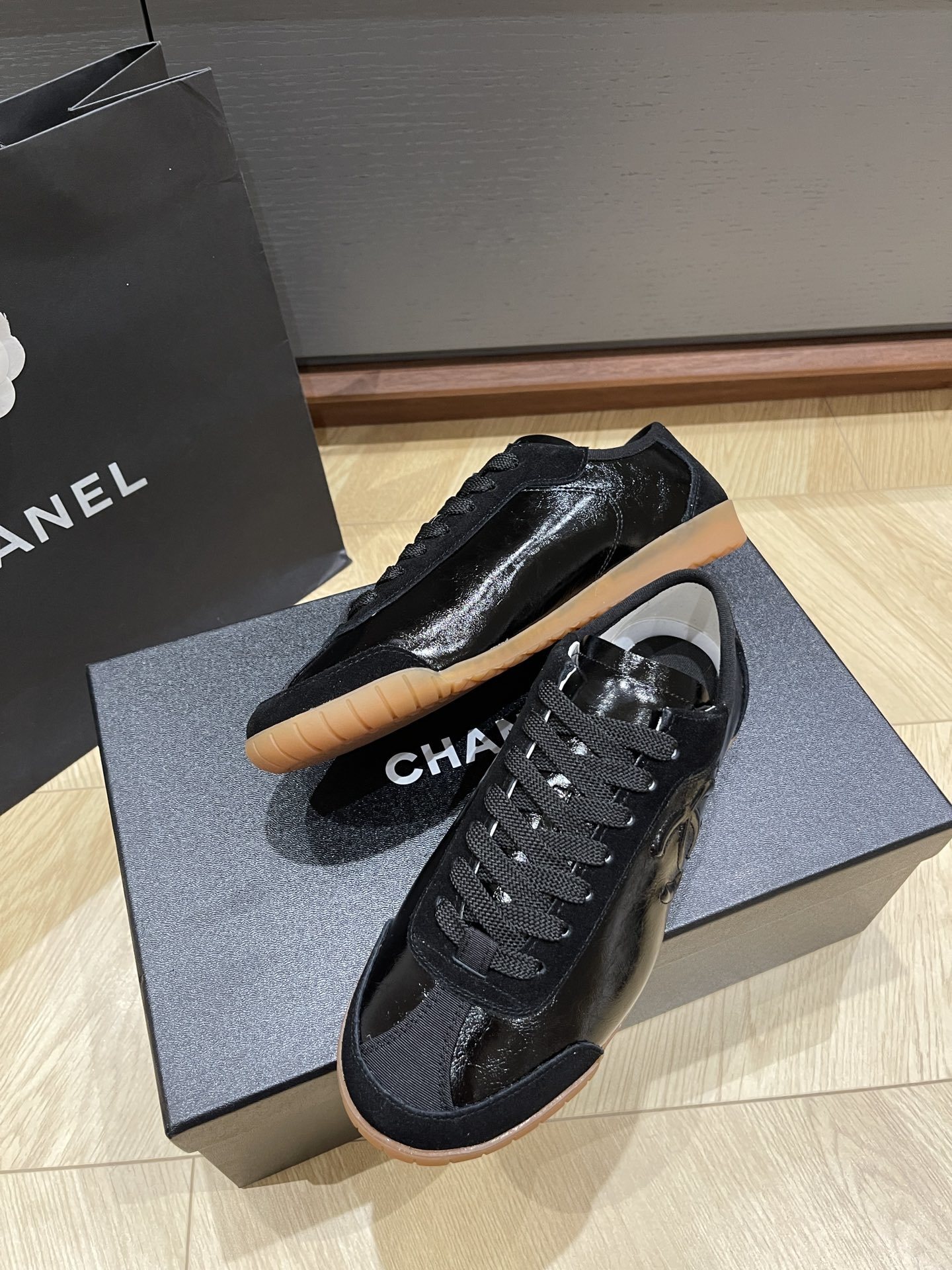 Pair of black Chanel sneakers in patent leather and suede with a gum sole, featuring the interlocking CC logo on the side. - Hình 3