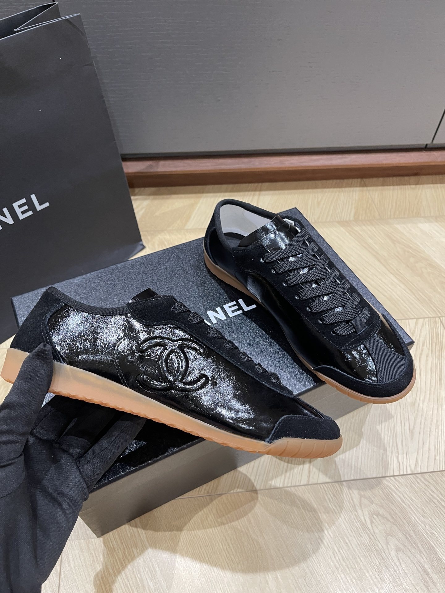 Pair of black Chanel sneakers in patent leather and suede with a gum sole, featuring the interlocking CC logo on the side. - Hình 2
