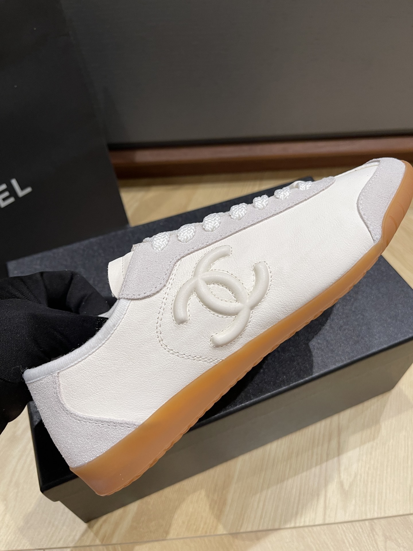 Chanel white calfskin and suede low-top sneakers with gum sole and CC logo resting on a black designer box. - Hình 7