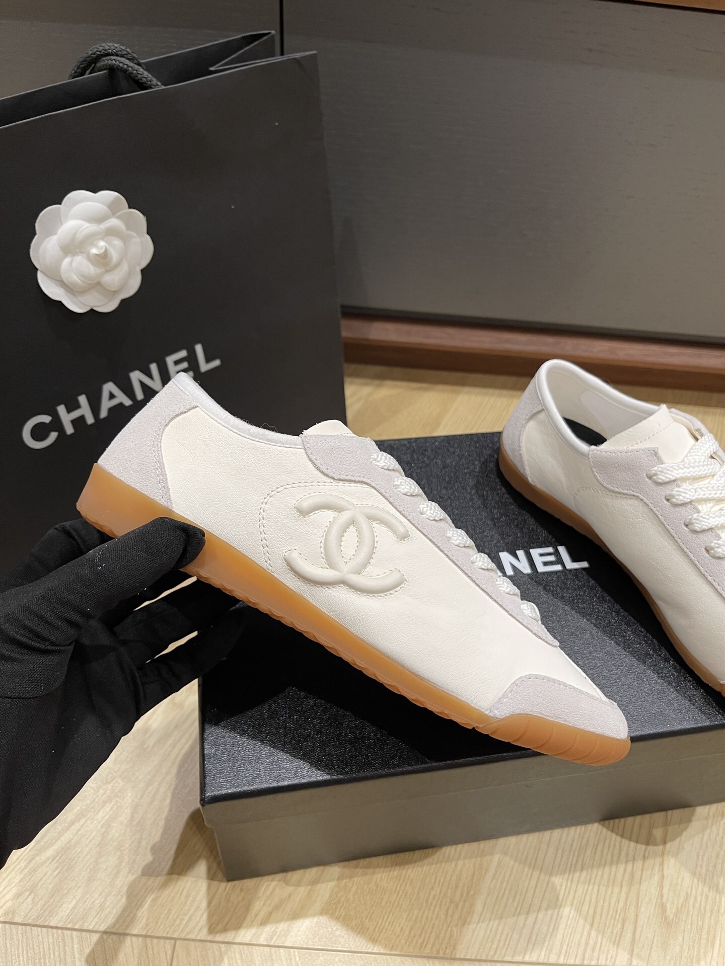 Chanel white calfskin and suede low-top sneakers with gum sole and CC logo resting on a black designer box. - Hình 3
