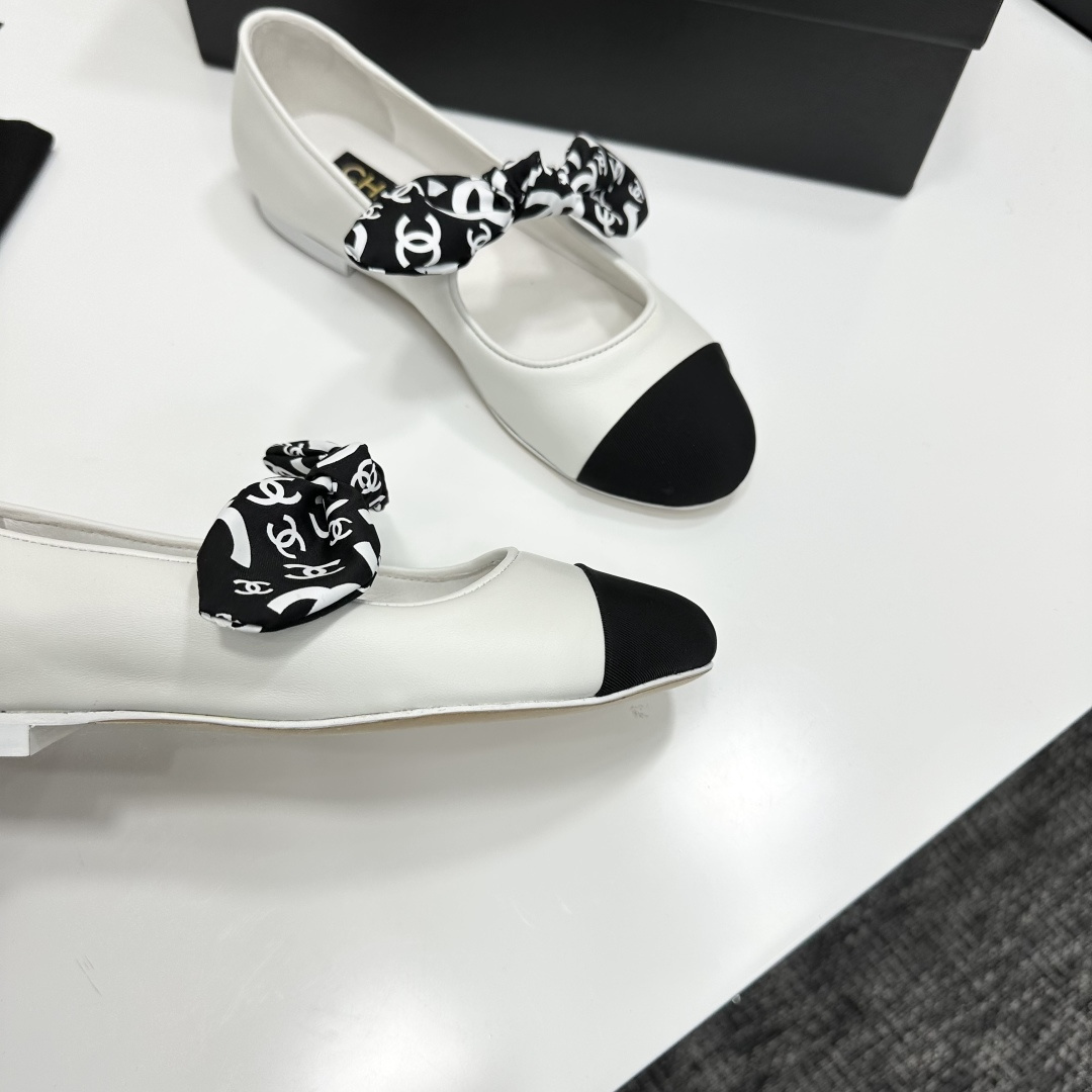 Elegant white leather ballet flats with a black cap toe and a printed CC logo bow detail resting on a black shoe box. - Hình 9