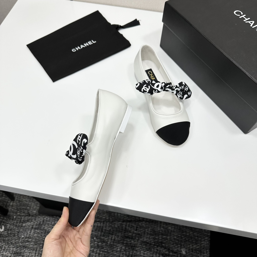 Elegant white leather ballet flats with a black cap toe and a printed CC logo bow detail resting on a black shoe box. - Hình 8