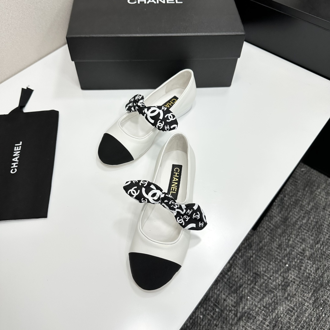 Elegant white leather ballet flats with a black cap toe and a printed CC logo bow detail resting on a black shoe box. - Hình 5